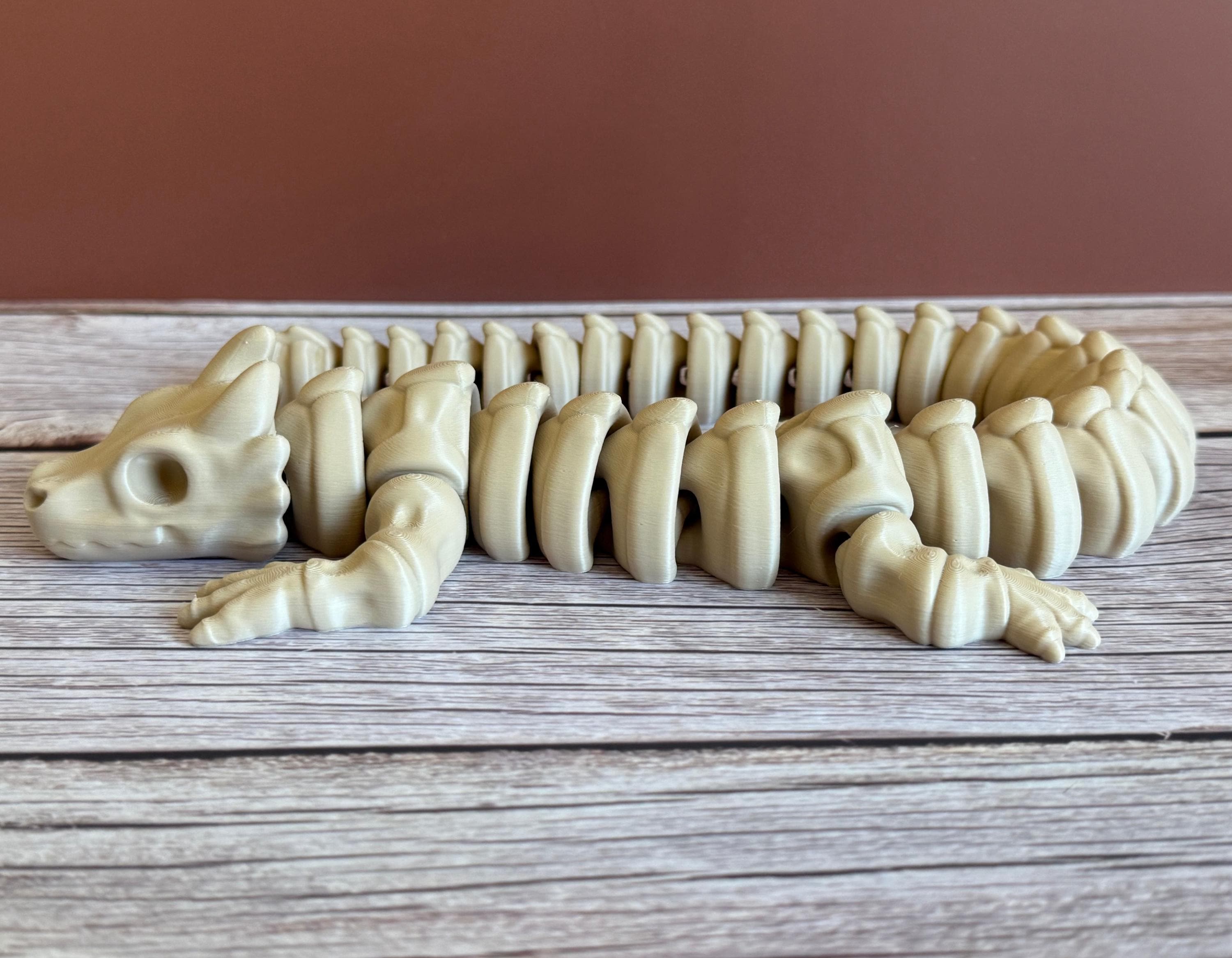Side of a 3D printed beige dragon skeleton toy, placed on a wooden surface