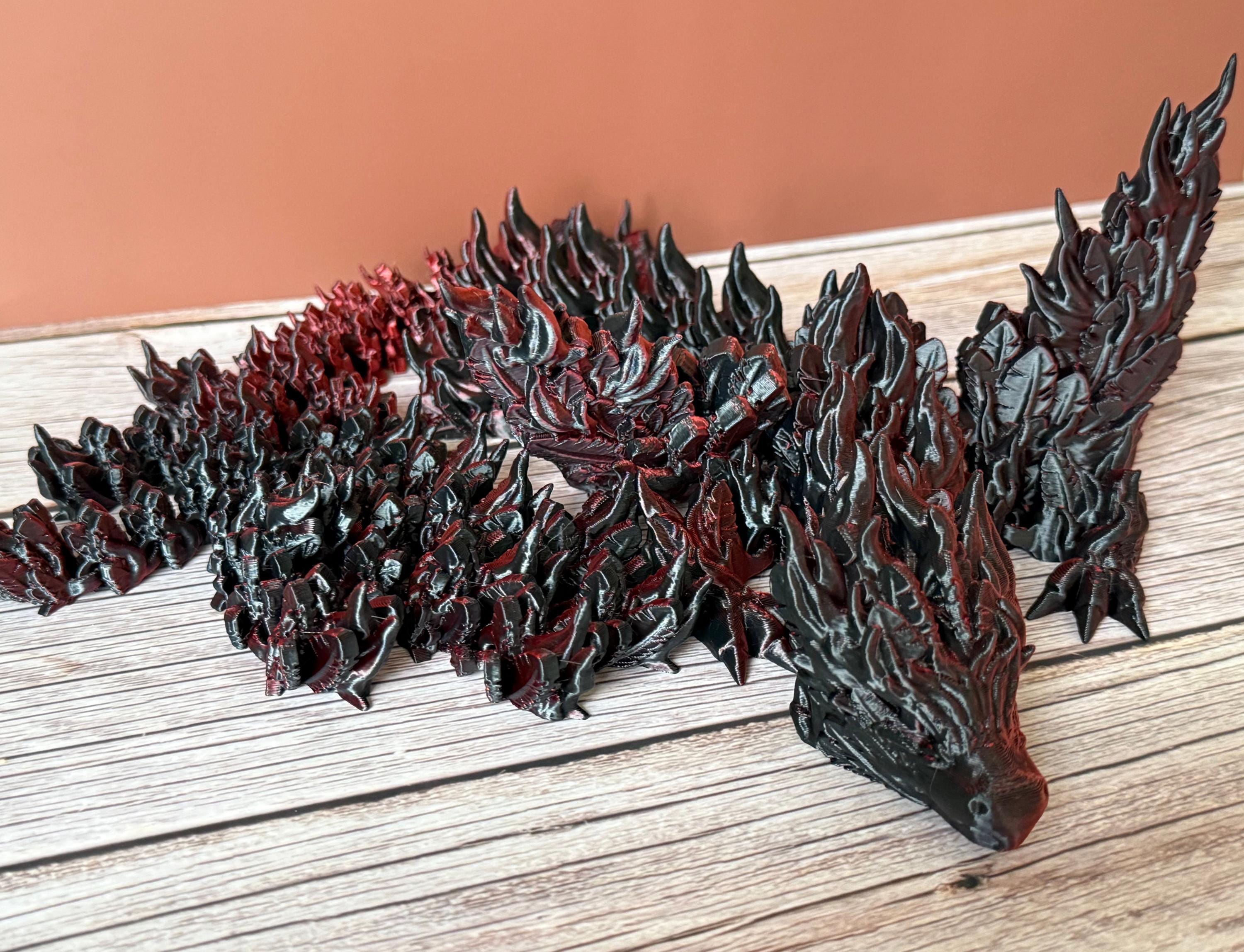 3D printed red and black dragon with flame-like features and wings, placed on a wooden surface