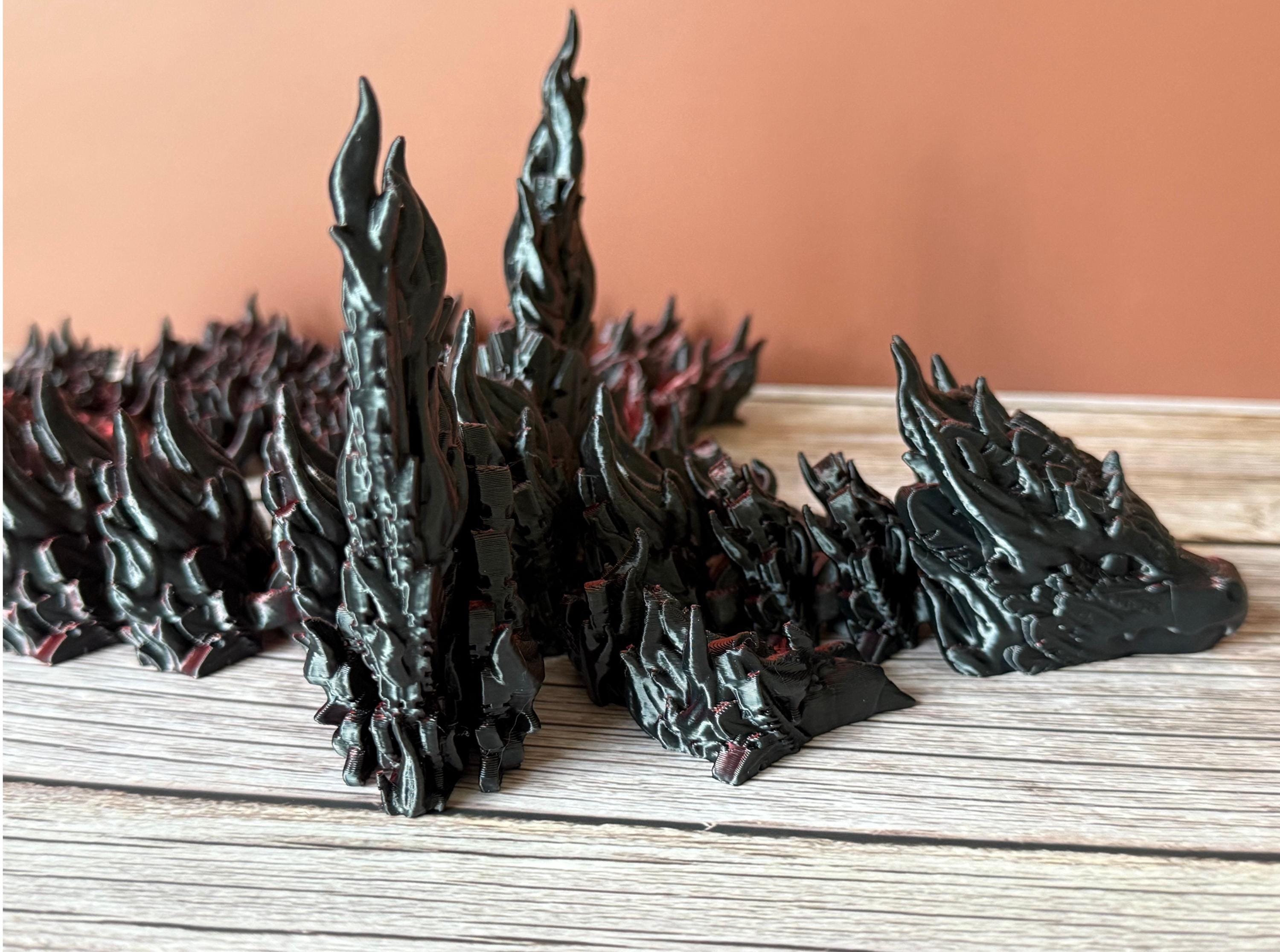 Side of a 3D printed red and black dragon with flame-like features and wings, placed on a wooden surface
