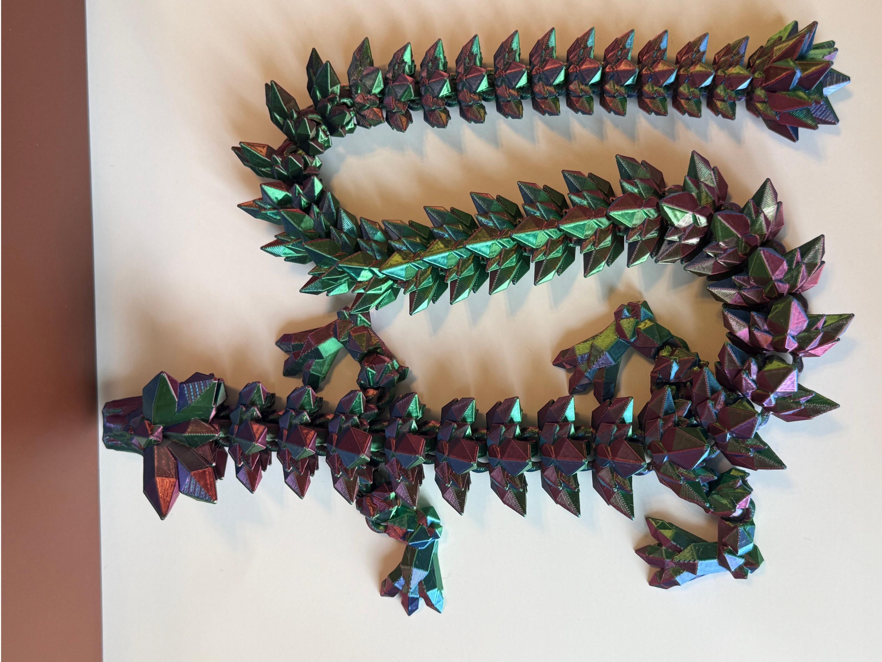 Multicolored 3D printed dragon with crystal-shaped features across the entire body, placed on a white surface 
