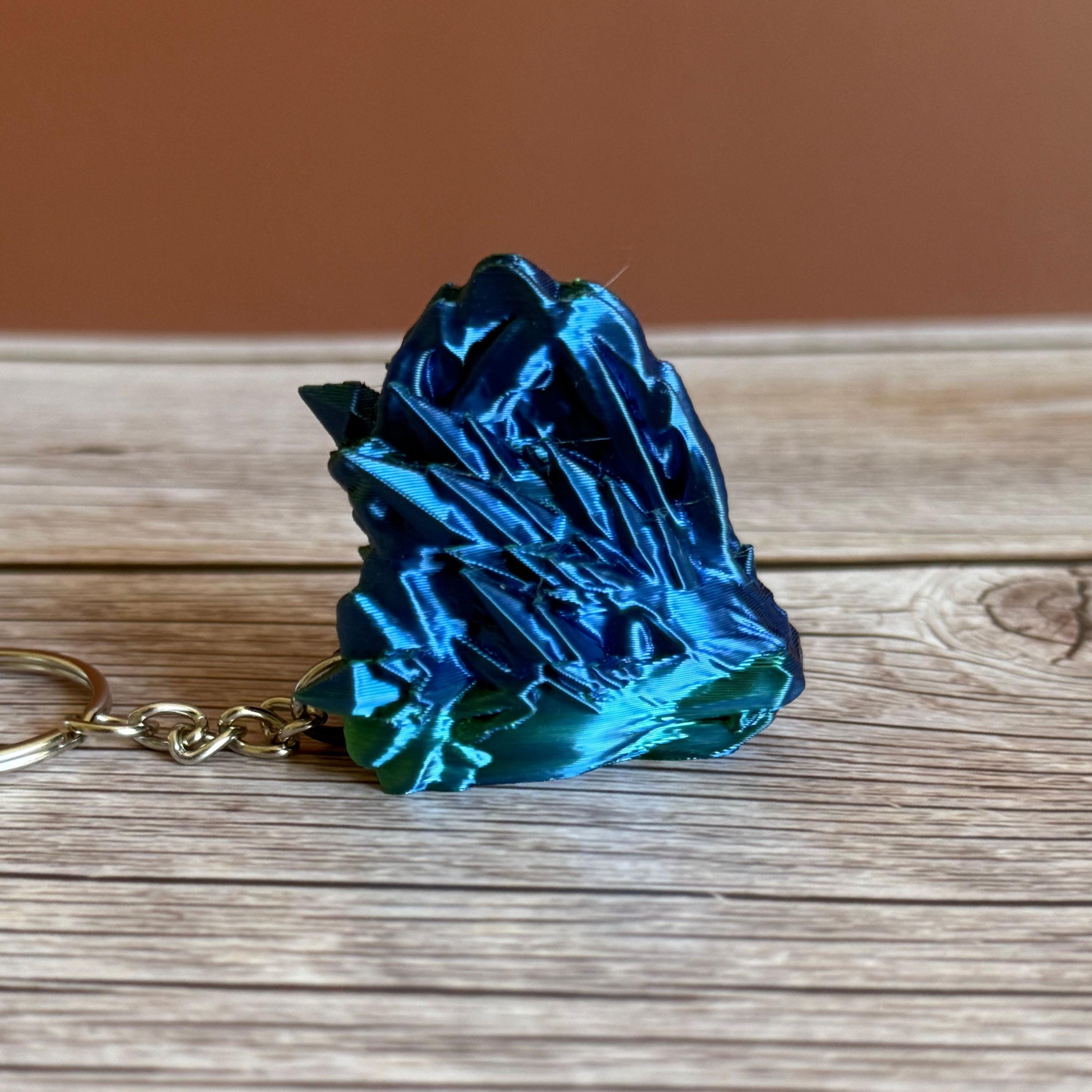 Side of a 3D printed blue and green jellyfish-themed dragon head keychain, placed on a wooden surface