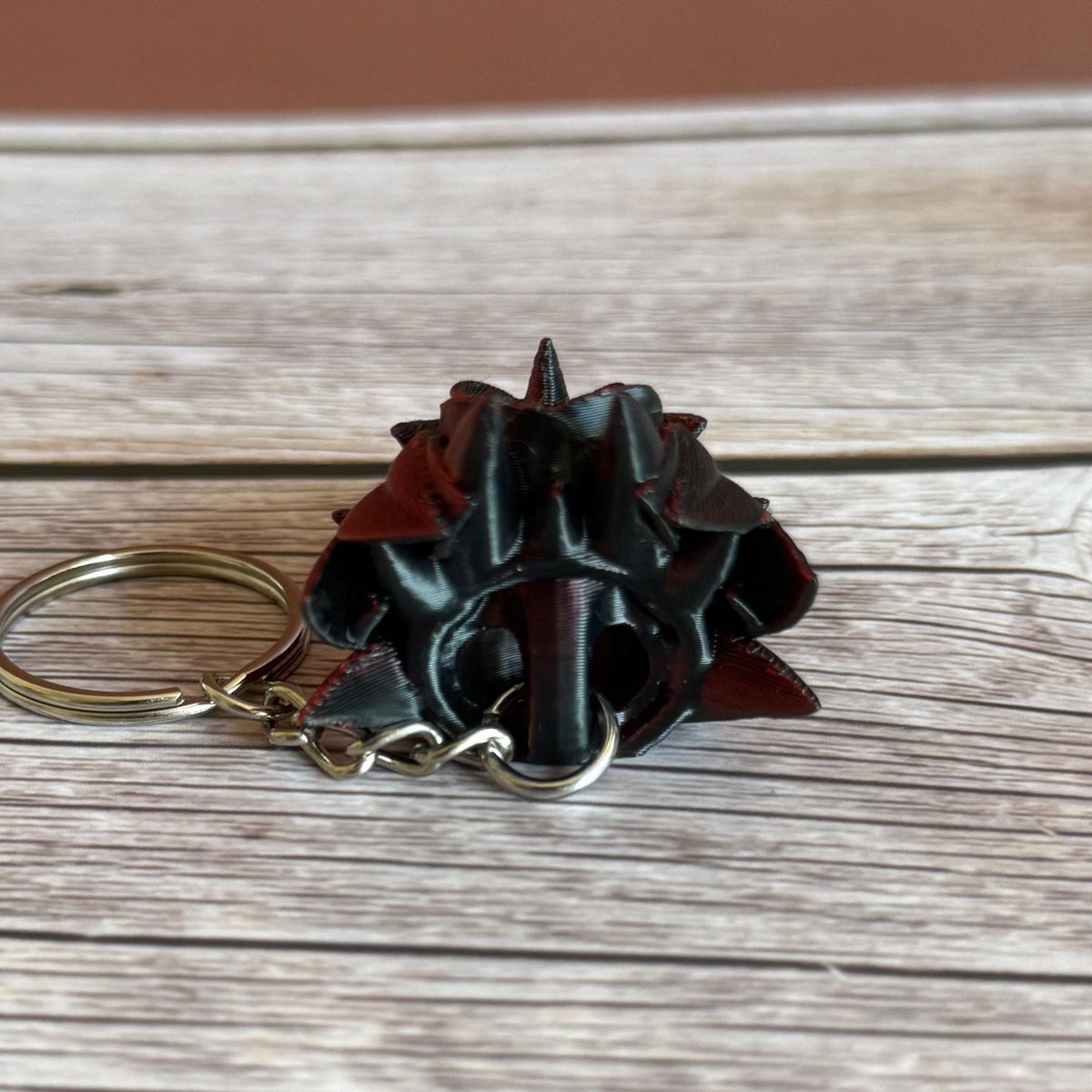 Back side of a 3D printed red and black dragon head keychain with a rose design on a wooden surface