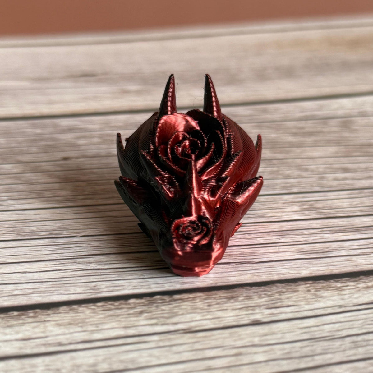 3D printed red and black dragon head keychain with a rose design on a wooden surface