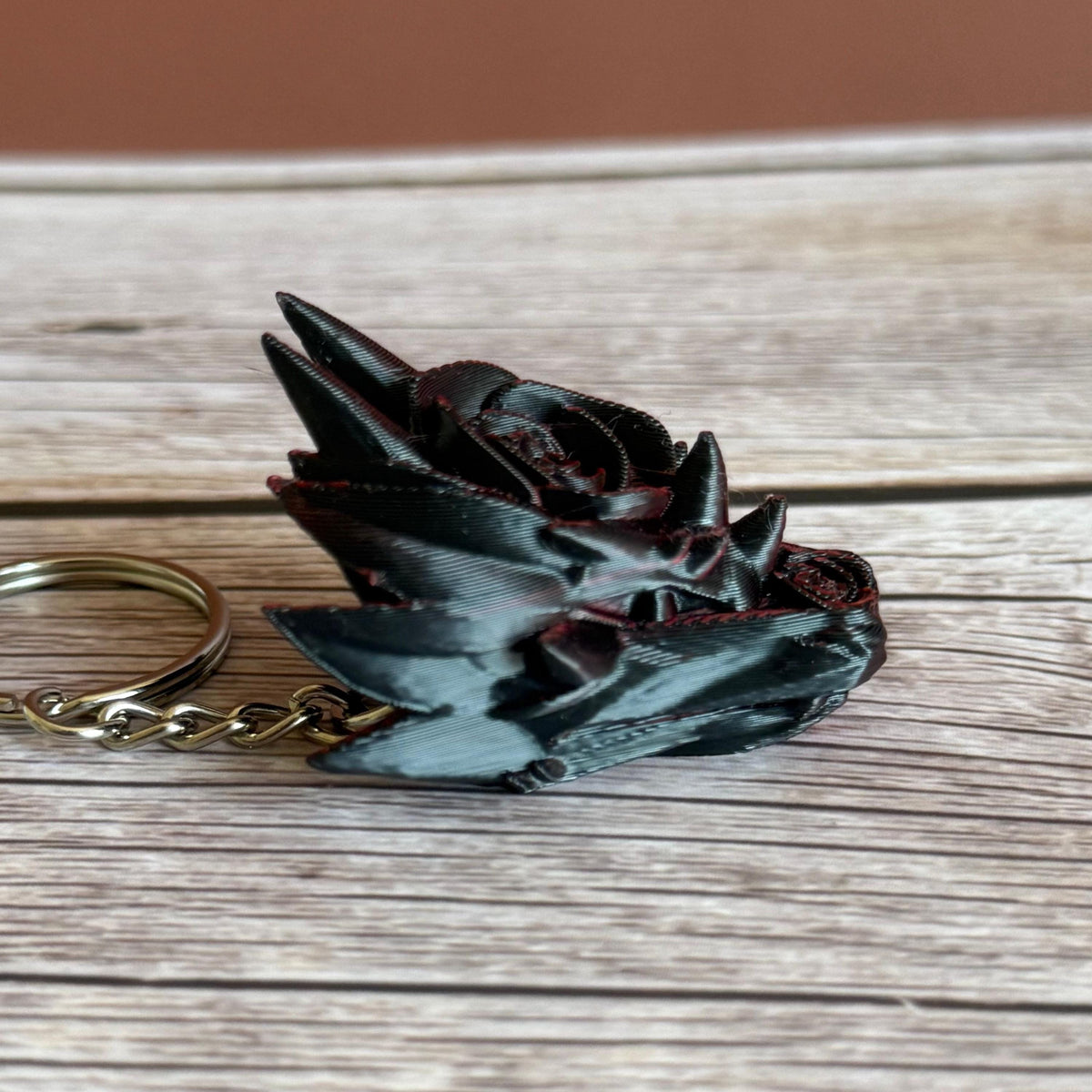 Primarily black side of a 3D printed red and black dragon head keychain with a rose design on a wooden surface