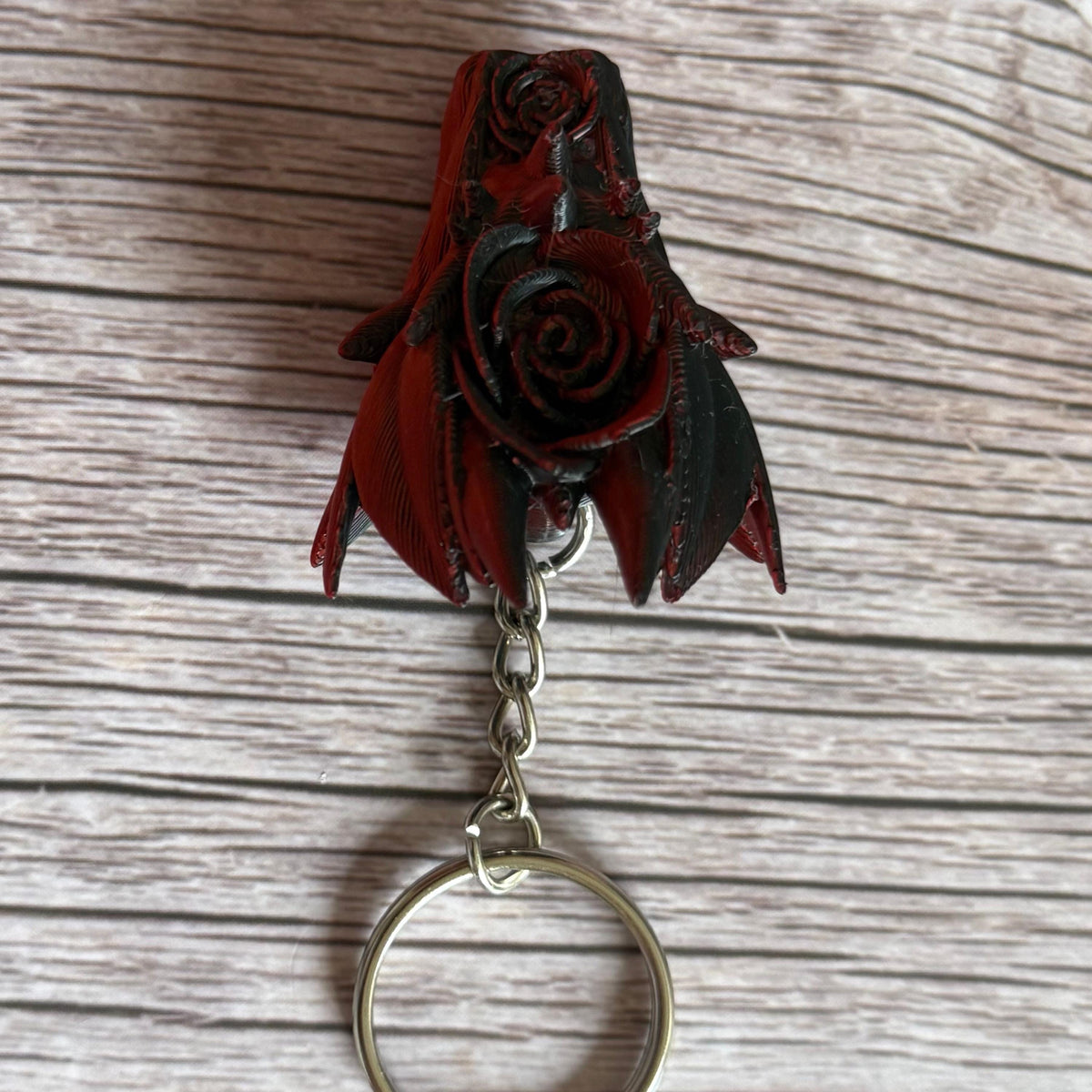 Top side of a 3D printed red and black dragon head keychain with a rose design on a wooden surface