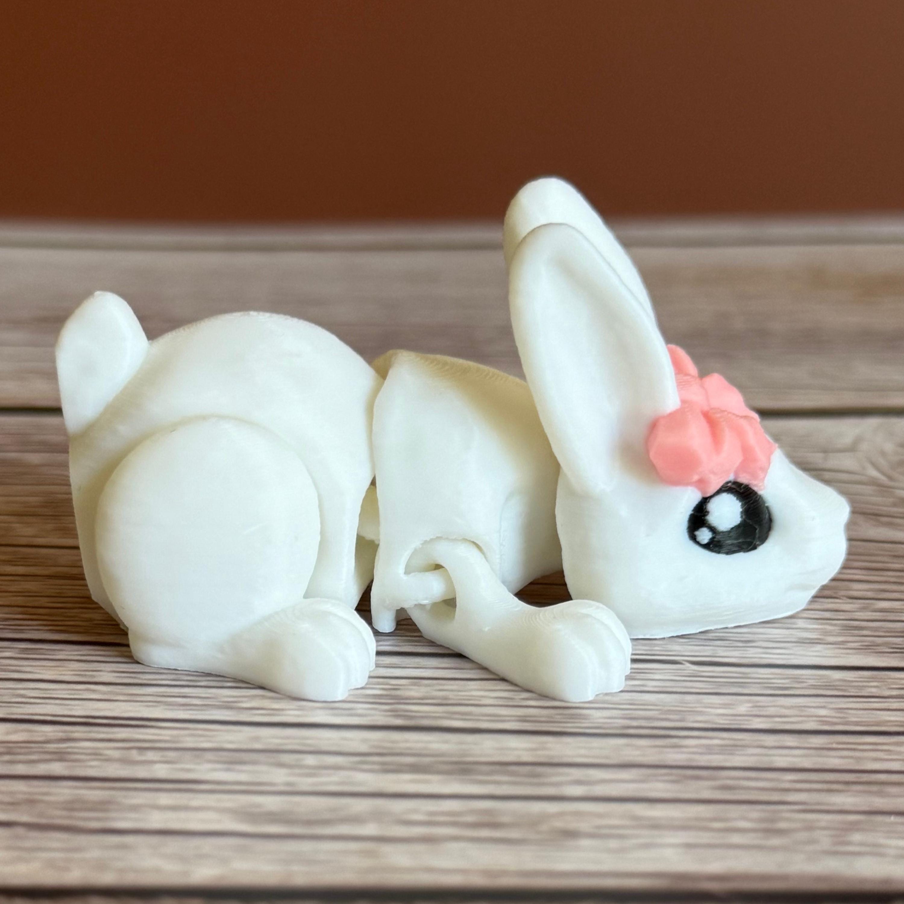 Side of a 3D printed white rabbit figurine with a pink bow on a wooden surface