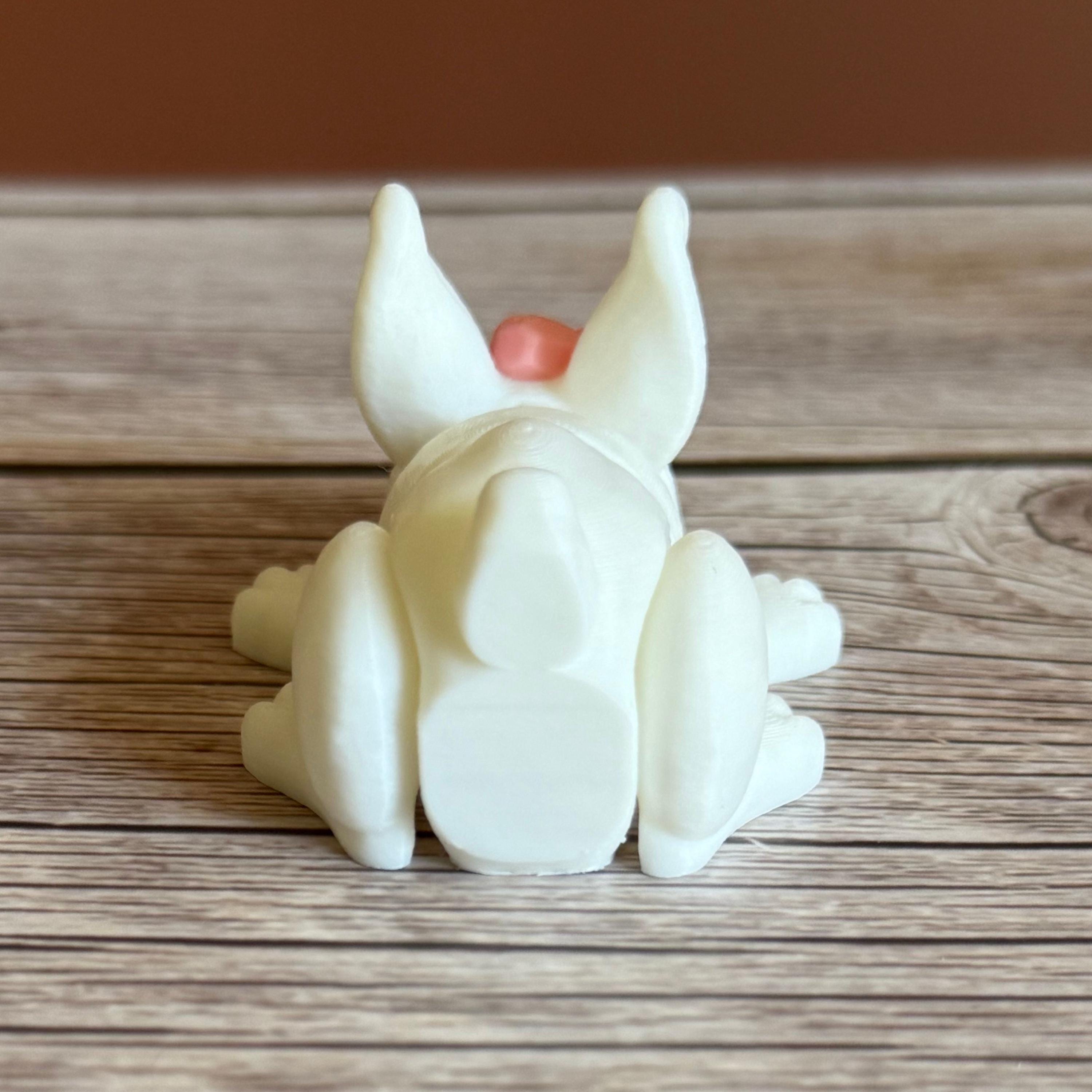 Back of a 3D printed white rabbit figurine with a pink bow on a wooden surface