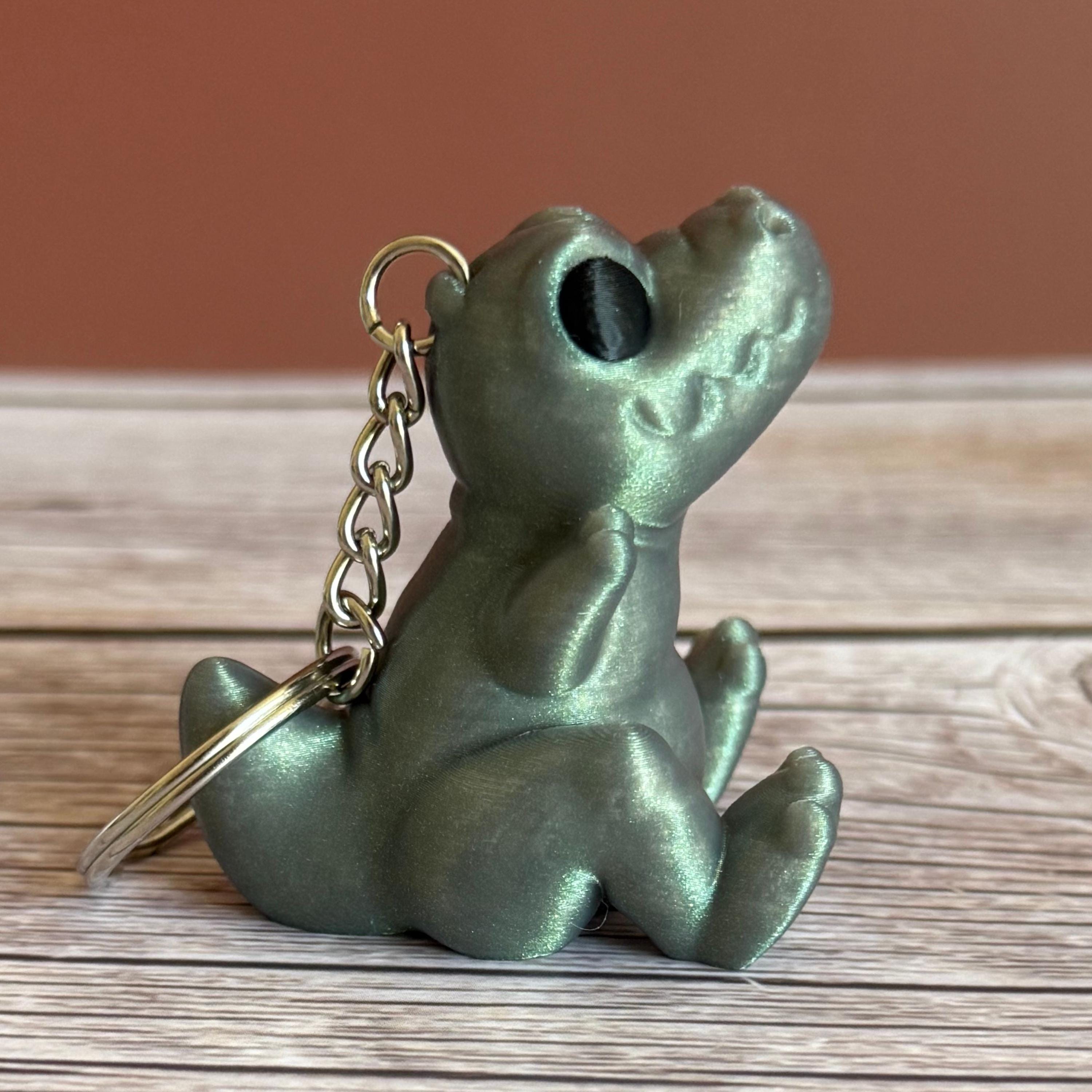 Side of a 3D printed shimmer-green T-Rex dinosaur keychain on a wooden surface
