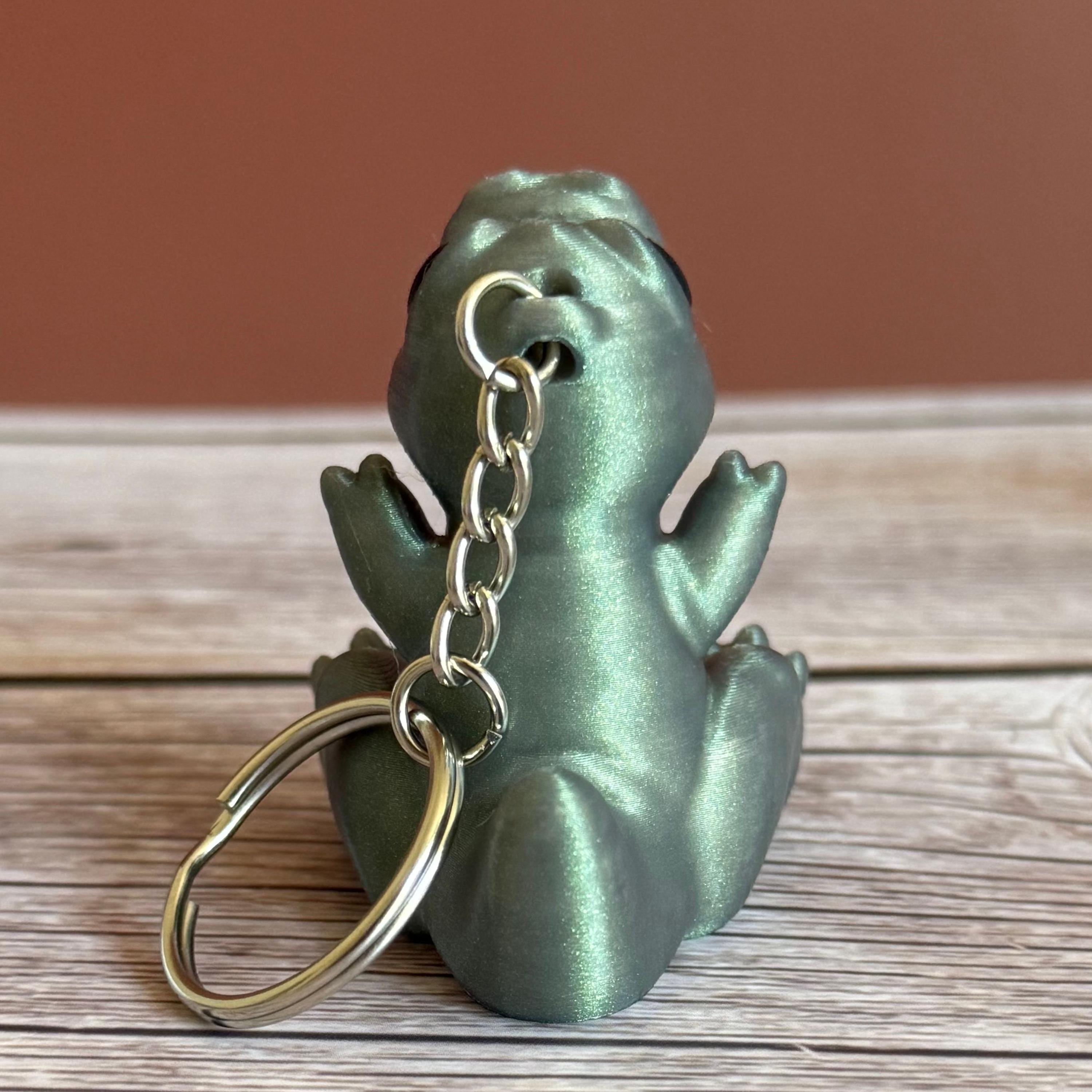 Back of a Side of a 3D printed shimmer-green T-Rex dinosaur keychain on a wooden surface