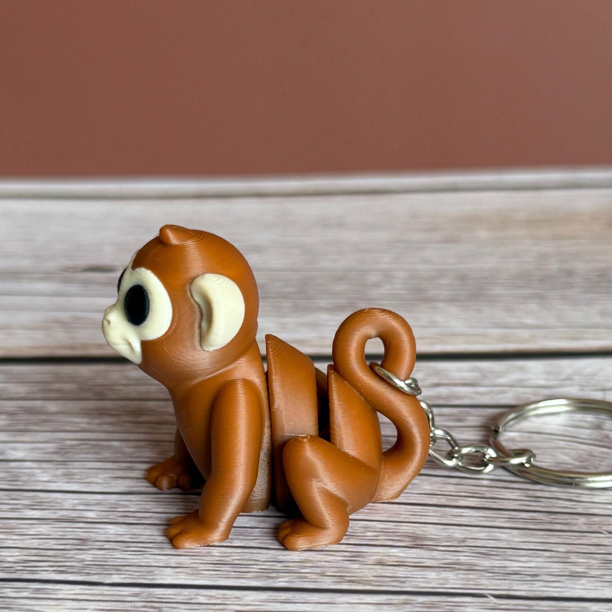 Side of a 3D printed brown monkey-shaped keychain on a wooden surface
