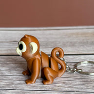 Side of a 3D printed brown monkey-shaped keychain on a wooden surface