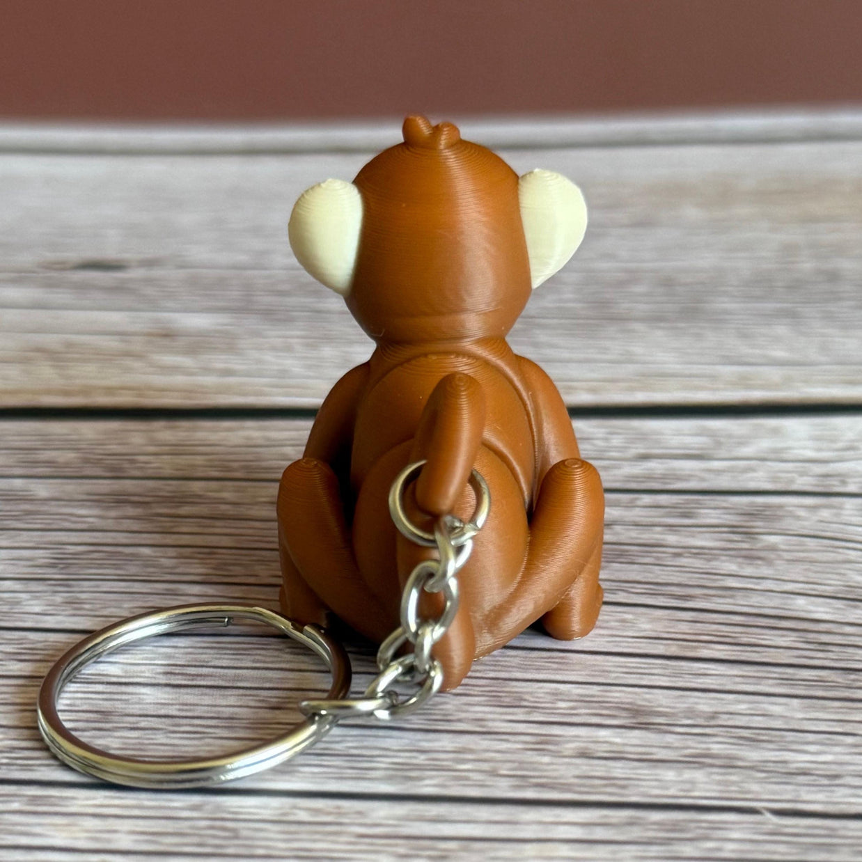 Back of a 3D printed brown monkey-shaped keychain on a wooden surface