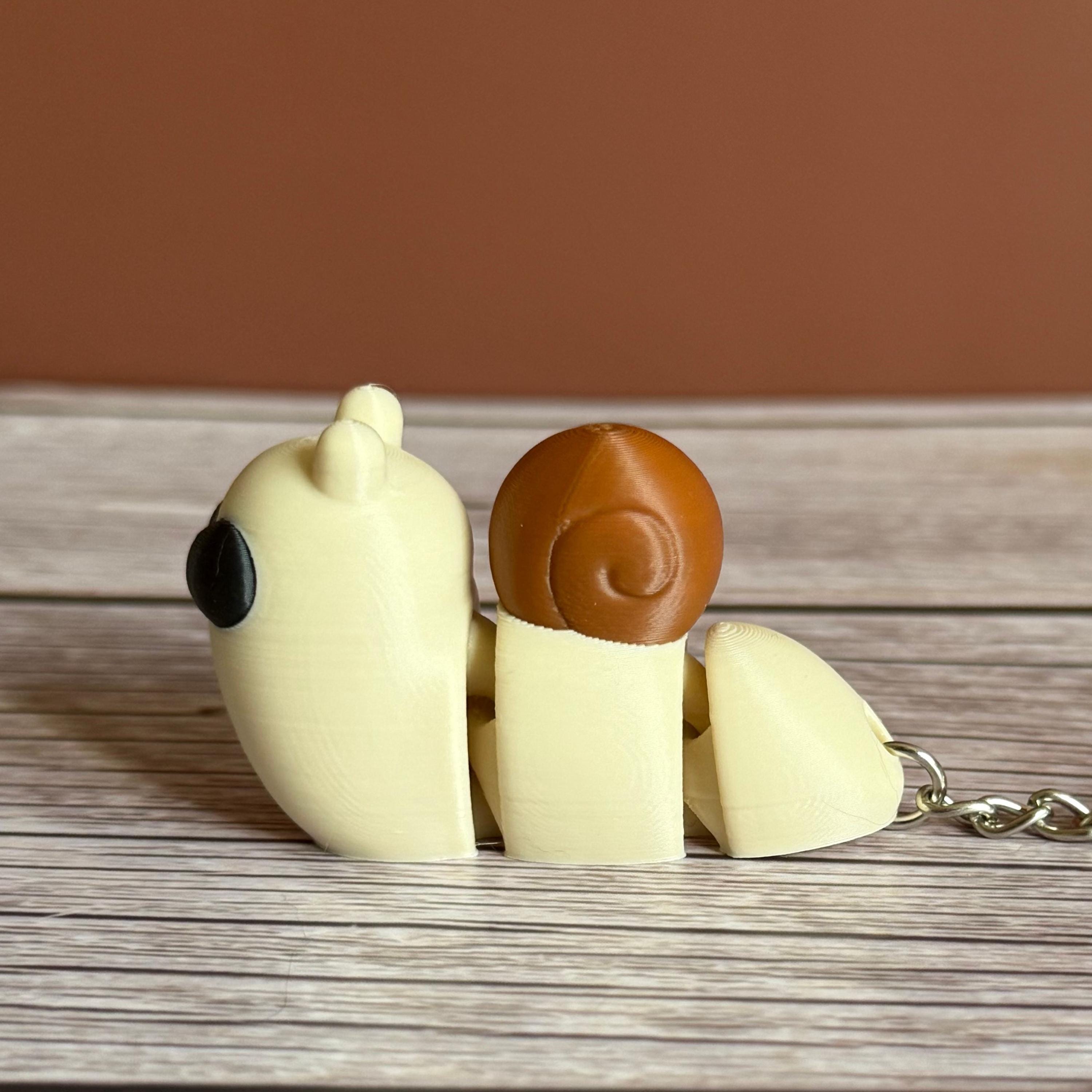 Side of a 3D printed beige and brown snail-shaped keychain on a wooden surface