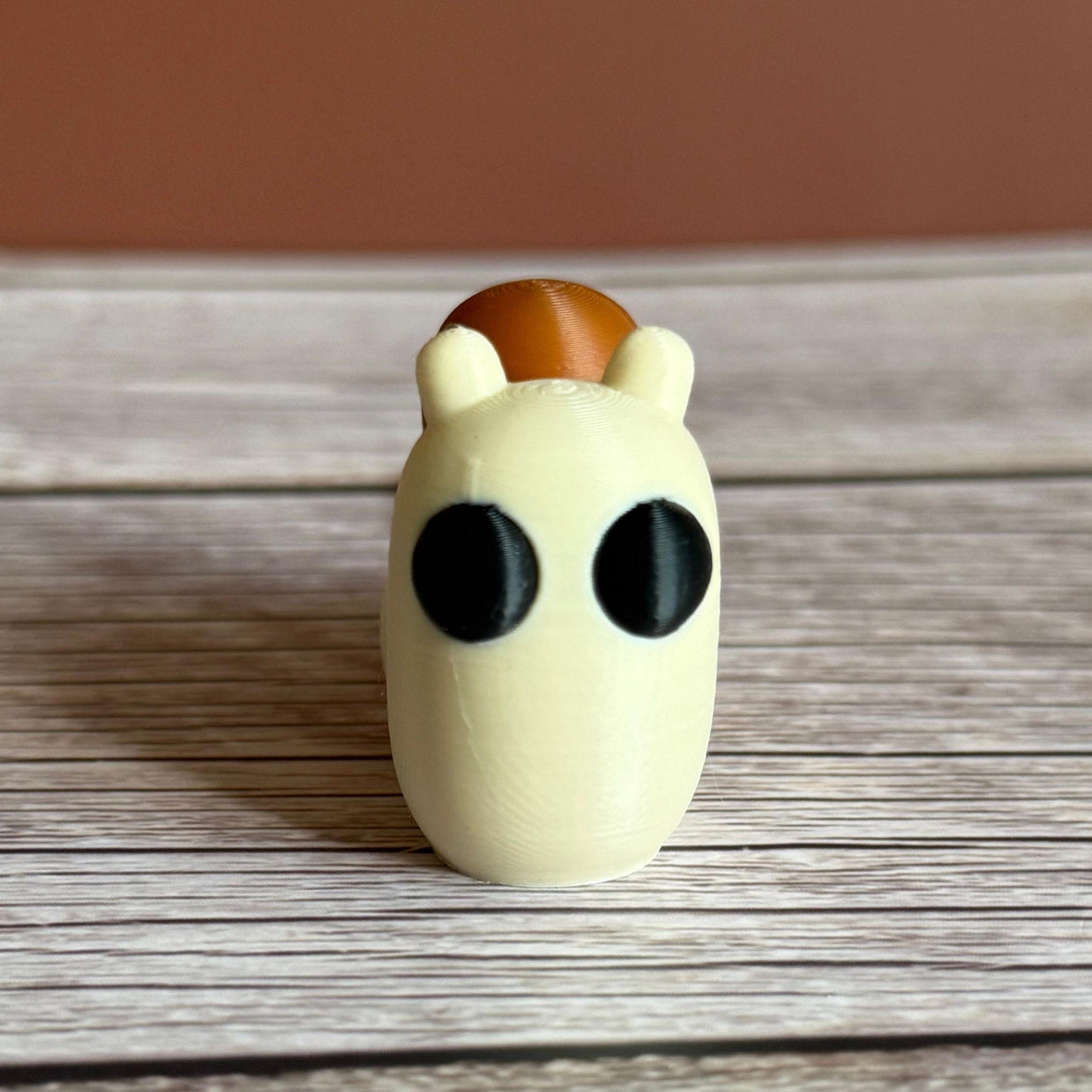 3D printed beige and brown snail-shaped keychain on a wooden surface