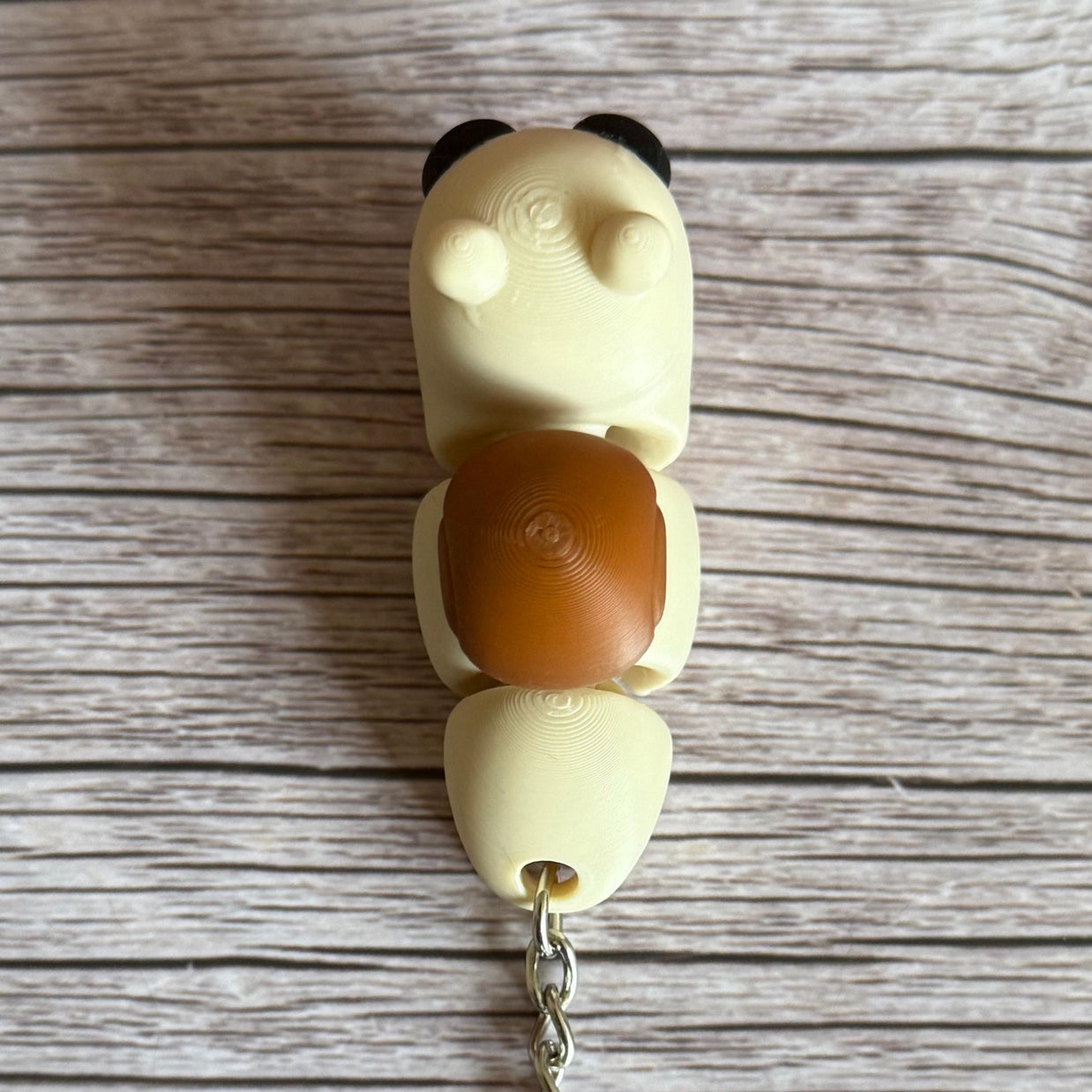 Top of a 3D printed beige and brown snail-shaped keychain on a wooden surface