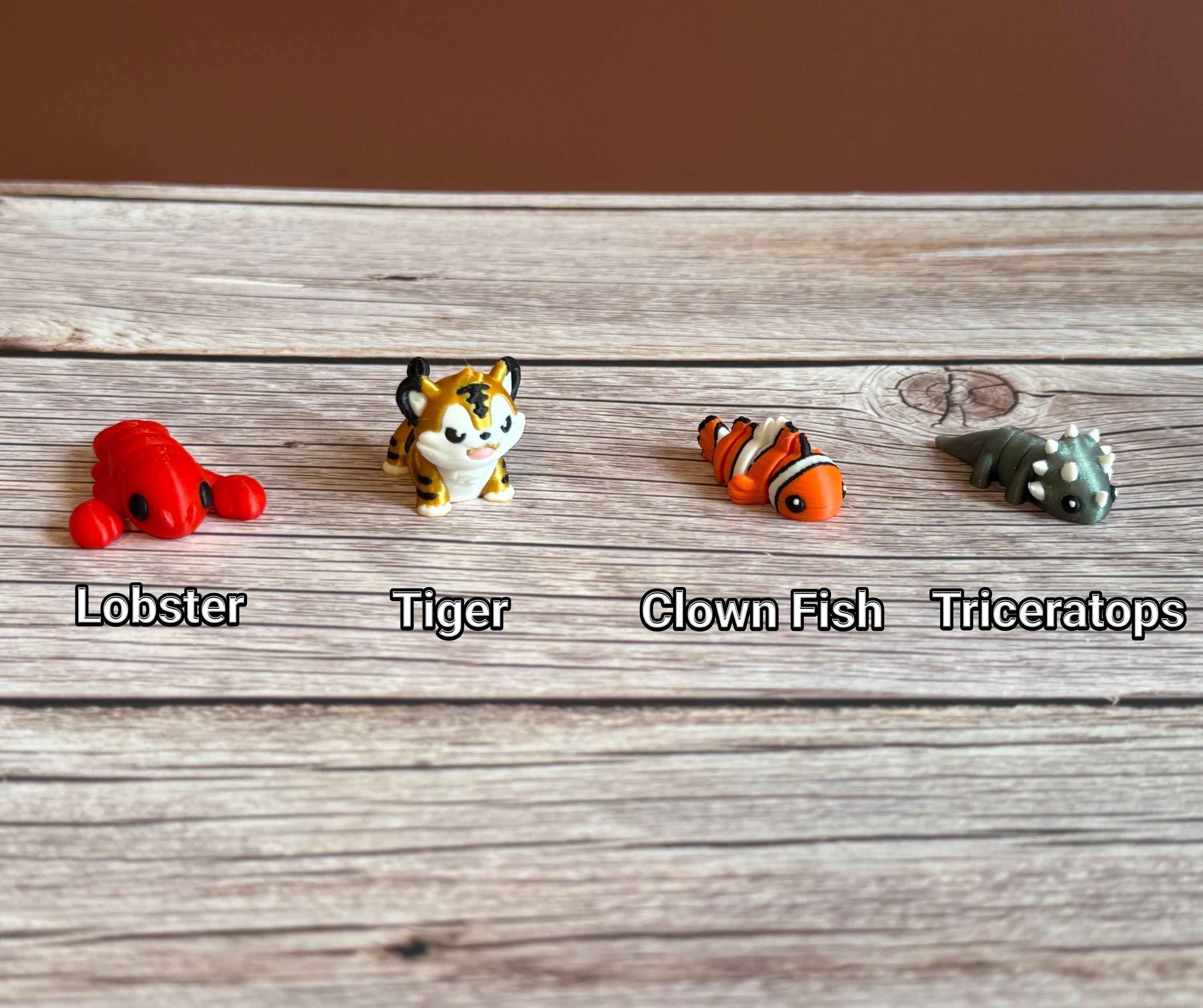 Collection of small animal figurines on a wooden surface. Tiger, lobster, triceratops, and clown fish are featured. 