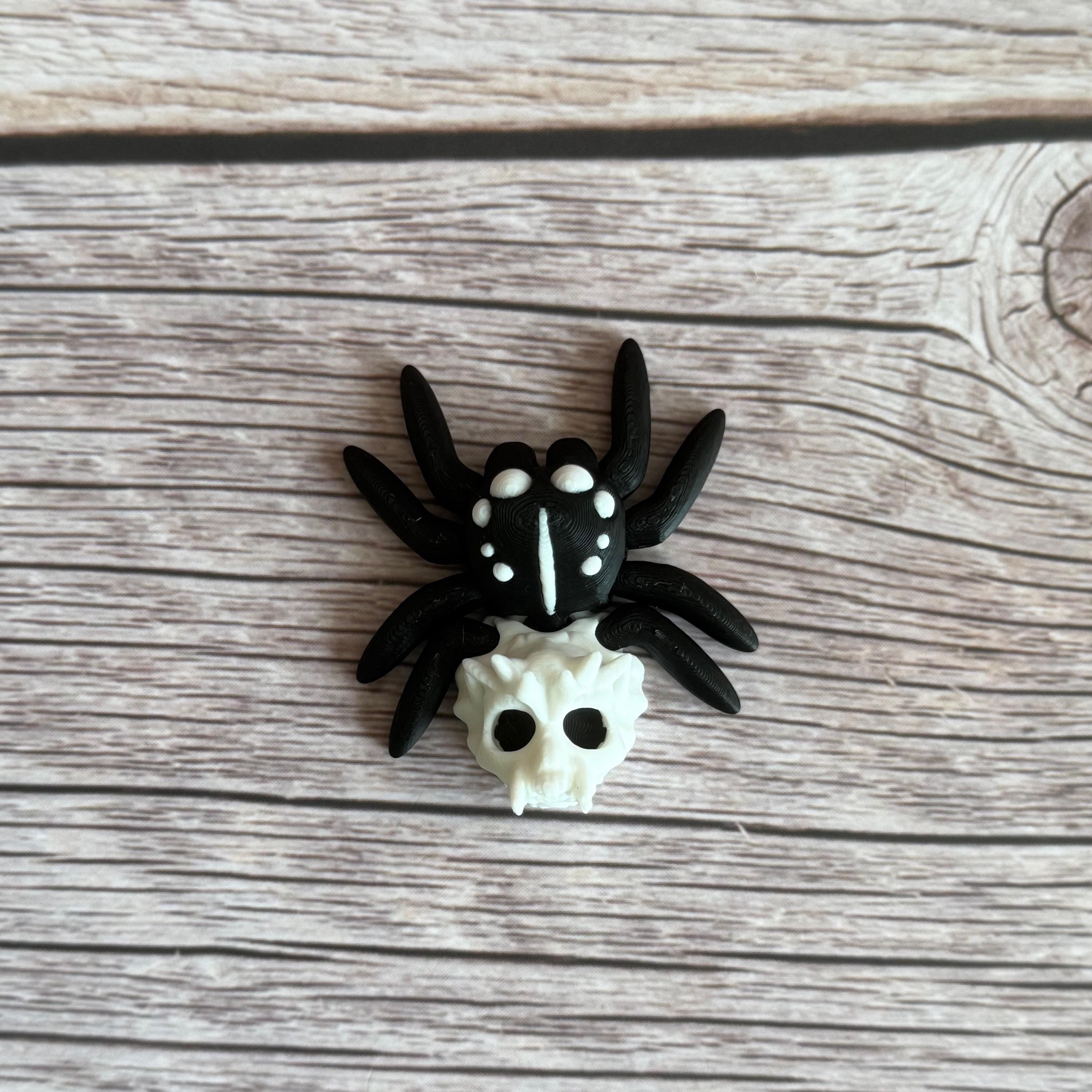 Black and white 3d printed spider featuring a skull on the backside, placed on a wooden surface