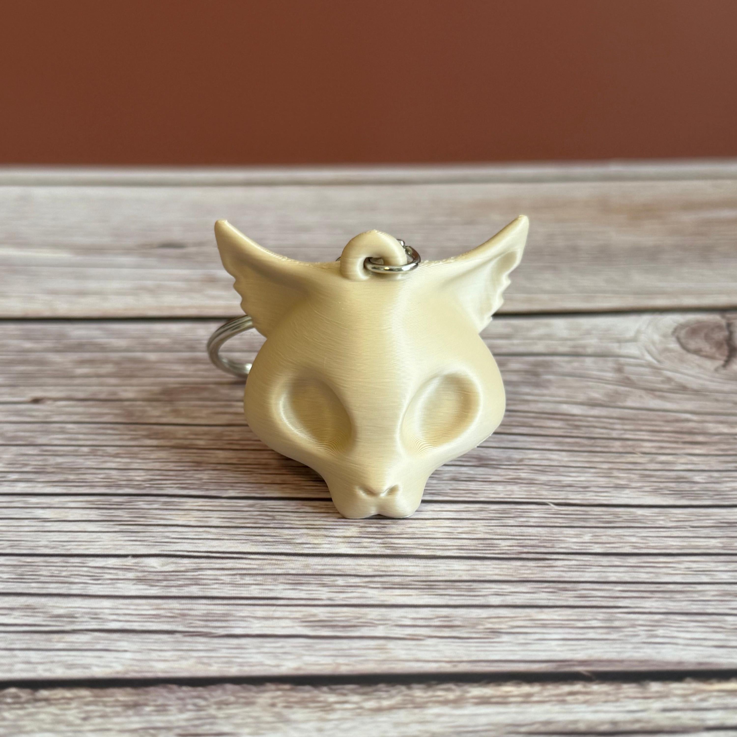 A 3D printed beige cat skull keychain on a wooden surface and brown backdrop
