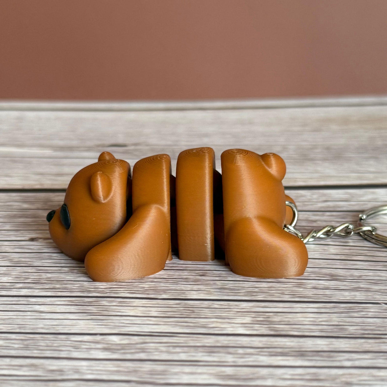 Side of a 3D printed brown bear-shaped keychain on a wooden surface