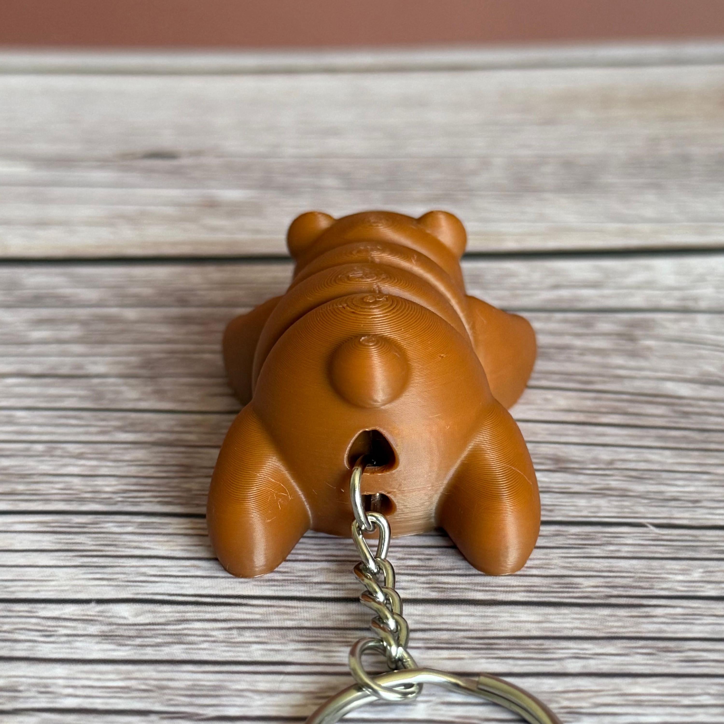 Back of a 3D printed brown bear-shaped keychain on a wooden surface