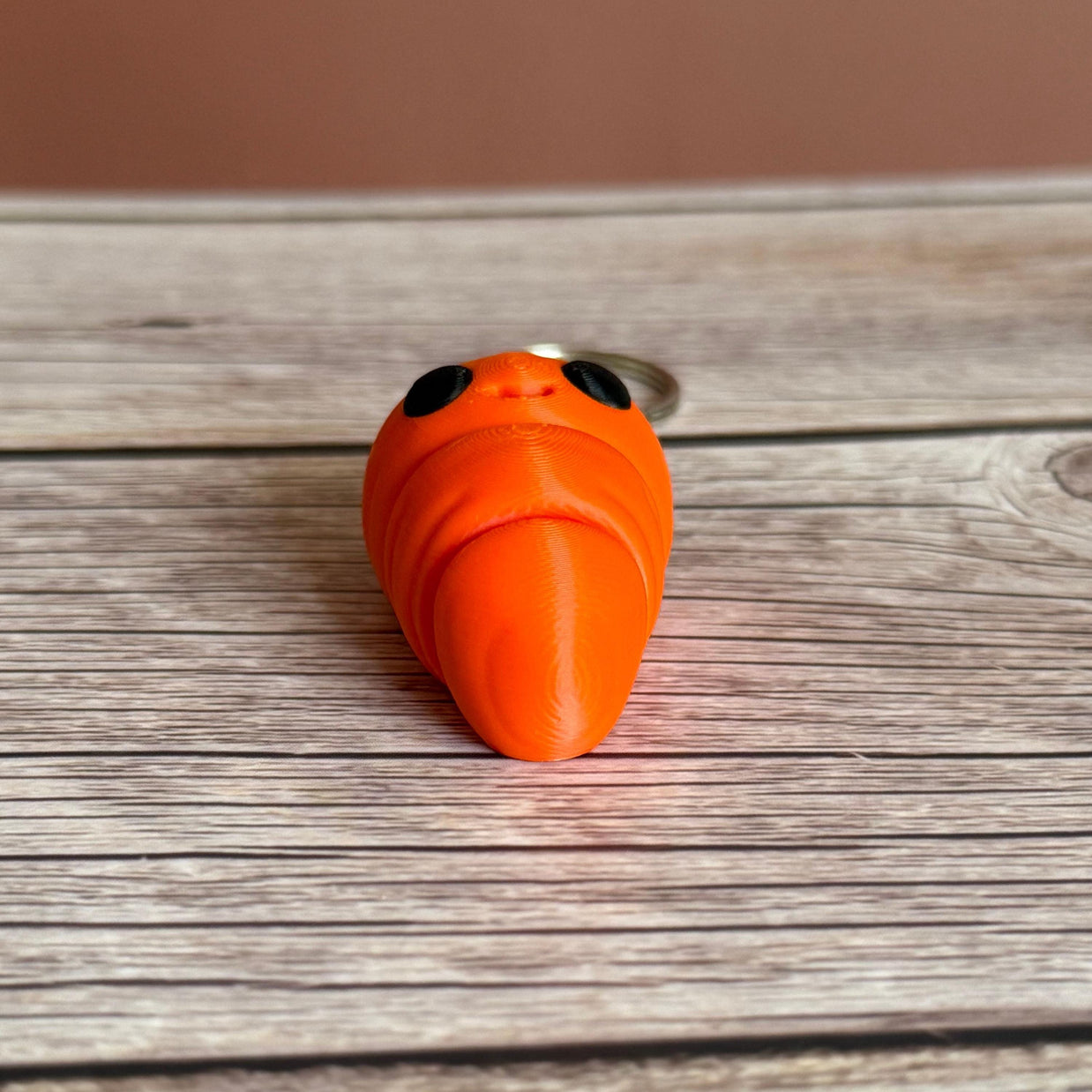 3D printed carrot-shaped keychain with a smiling face on a wooden surface