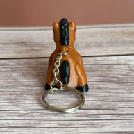 Back of a 3D printed brown and black horse-shaped keychain on a wooden surface