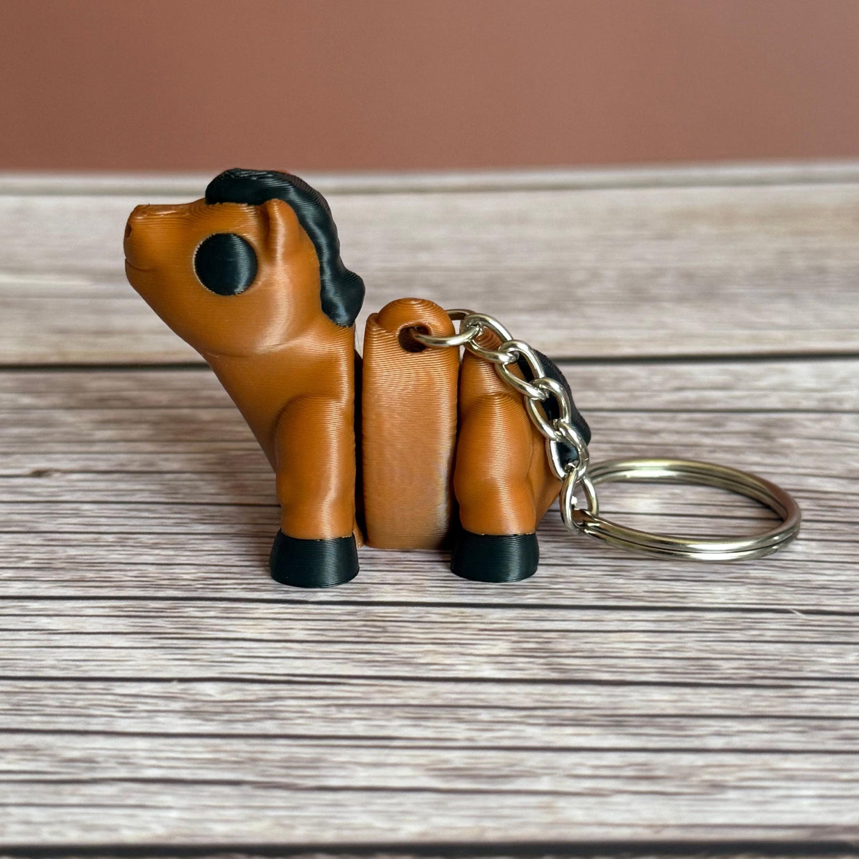 Side of a 3D printed brown and black horse-shaped keychain on a wooden surface