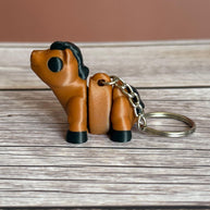Side of a 3D printed brown and black horse-shaped keychain on a wooden surface