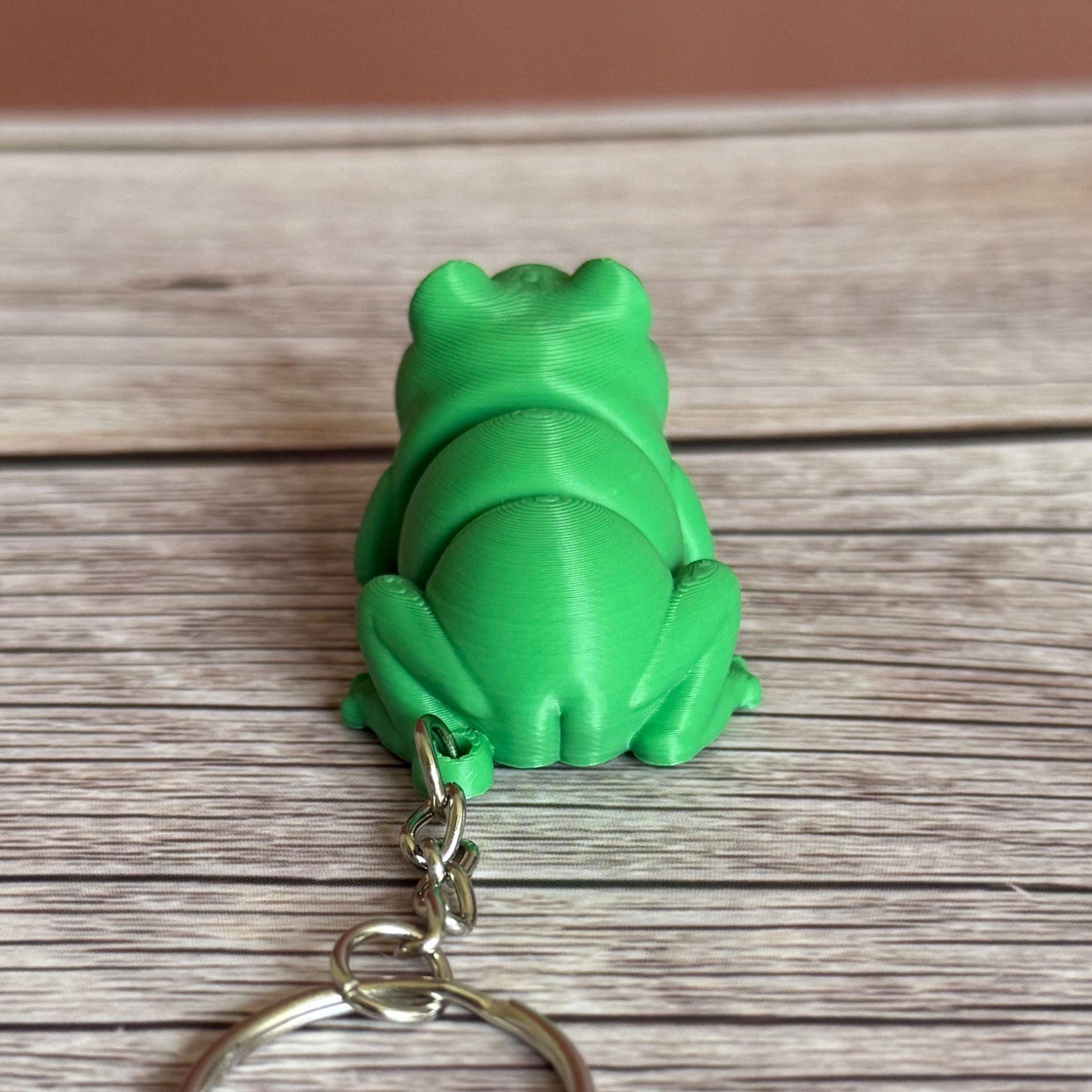 Back of a 3D printed green frog-shaped keychain on a wooden surface