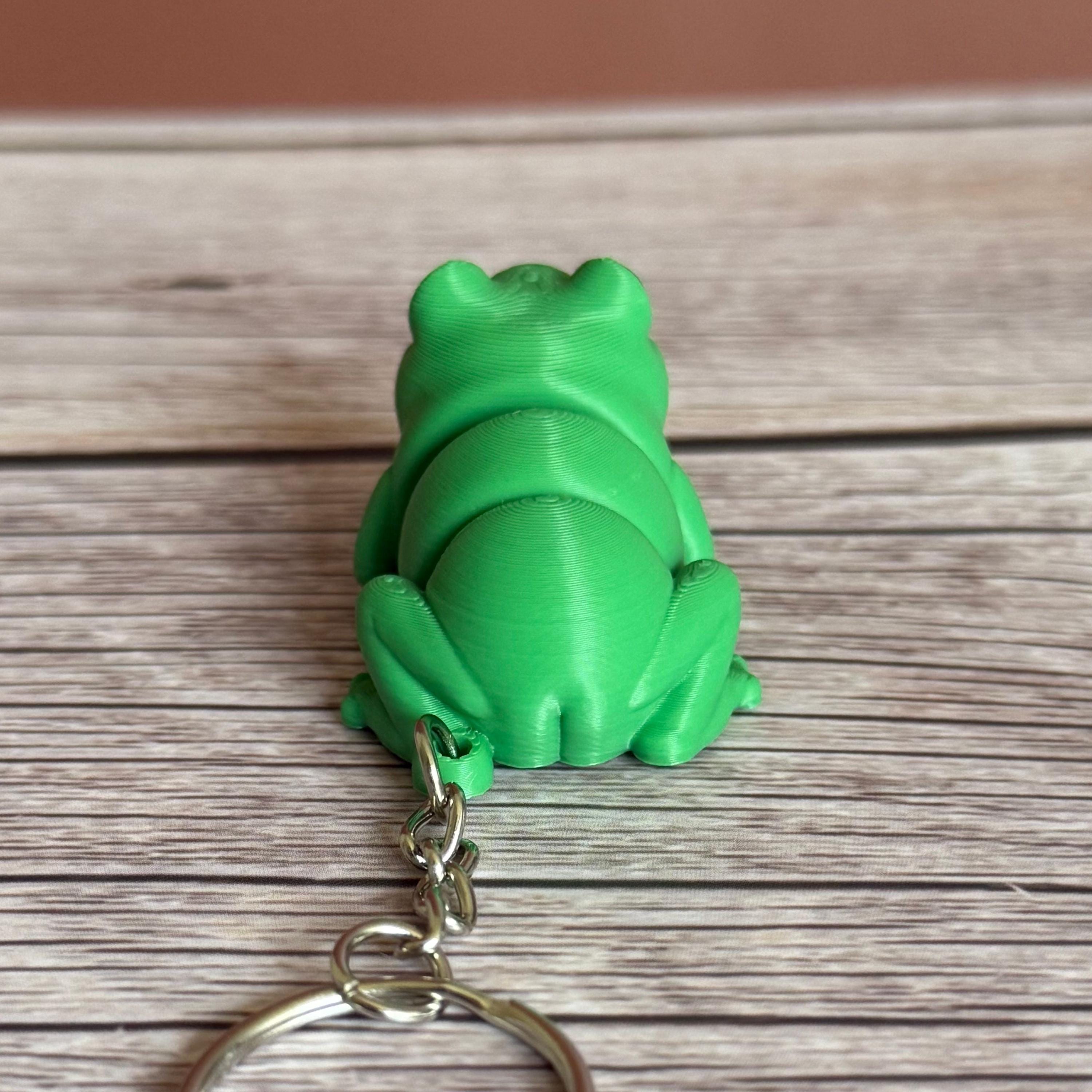 Back of a 3D printed green frog-shaped keychain on a wooden surface