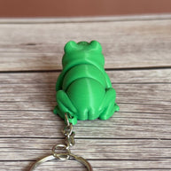 Back of a 3D printed green frog-shaped keychain on a wooden surface