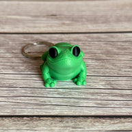 3D printed green frog-shaped keychain on a wooden surface