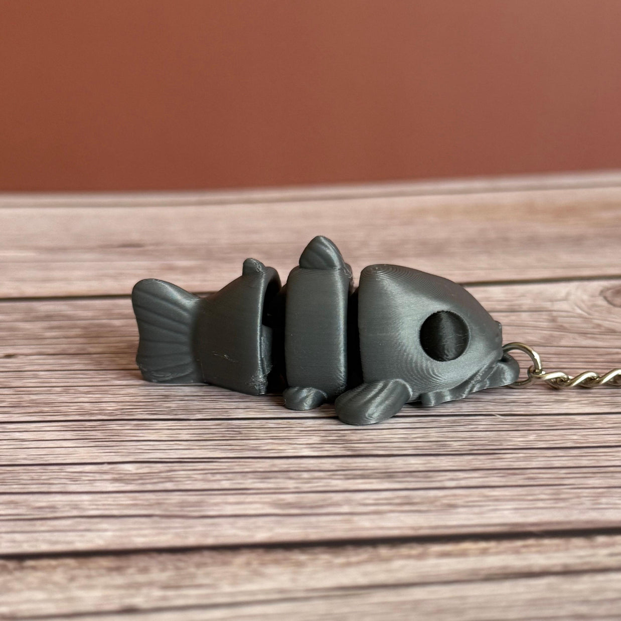 Side of a 3D printed gray catfish-shaped keychain on a wooden surface