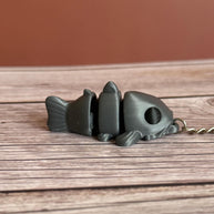 Side of a 3D printed gray catfish-shaped keychain on a wooden surface