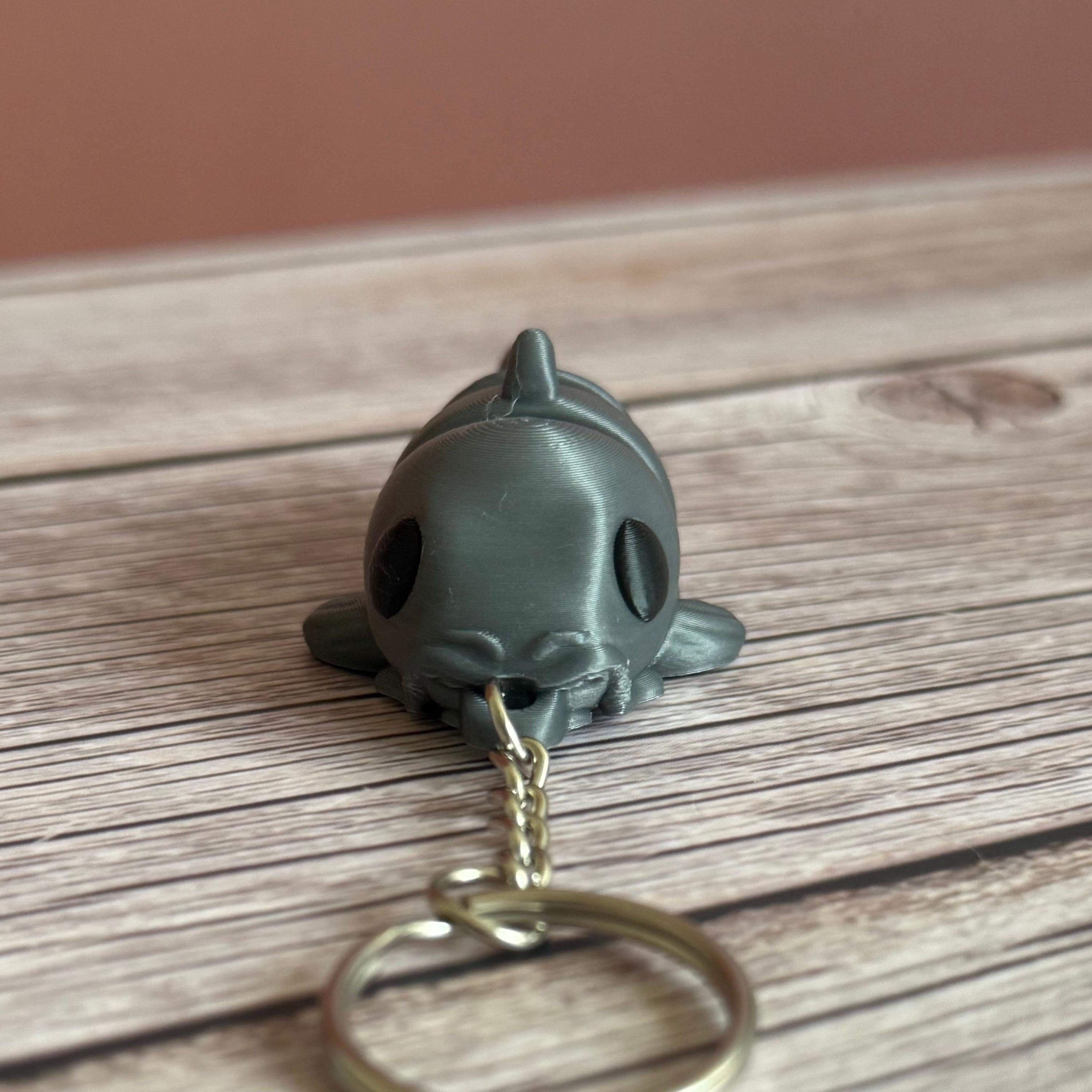 3D printed gray catfish-shaped keychain on a wooden surface