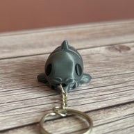 3D printed gray catfish-shaped keychain on a wooden surface