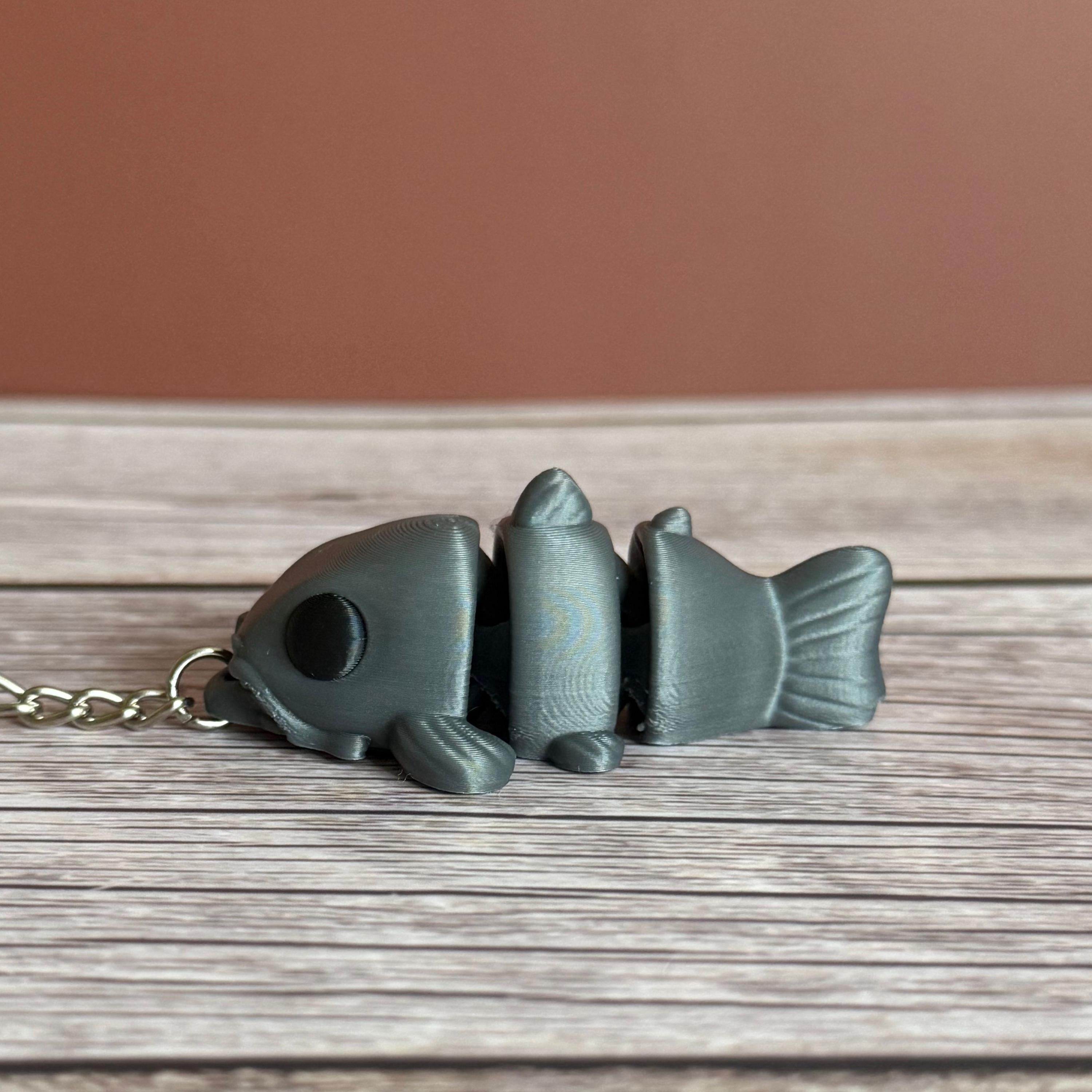 side of a 3D printed gray catfish-shaped keychain on a wooden surface