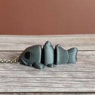 side of a 3D printed gray catfish-shaped keychain on a wooden surface