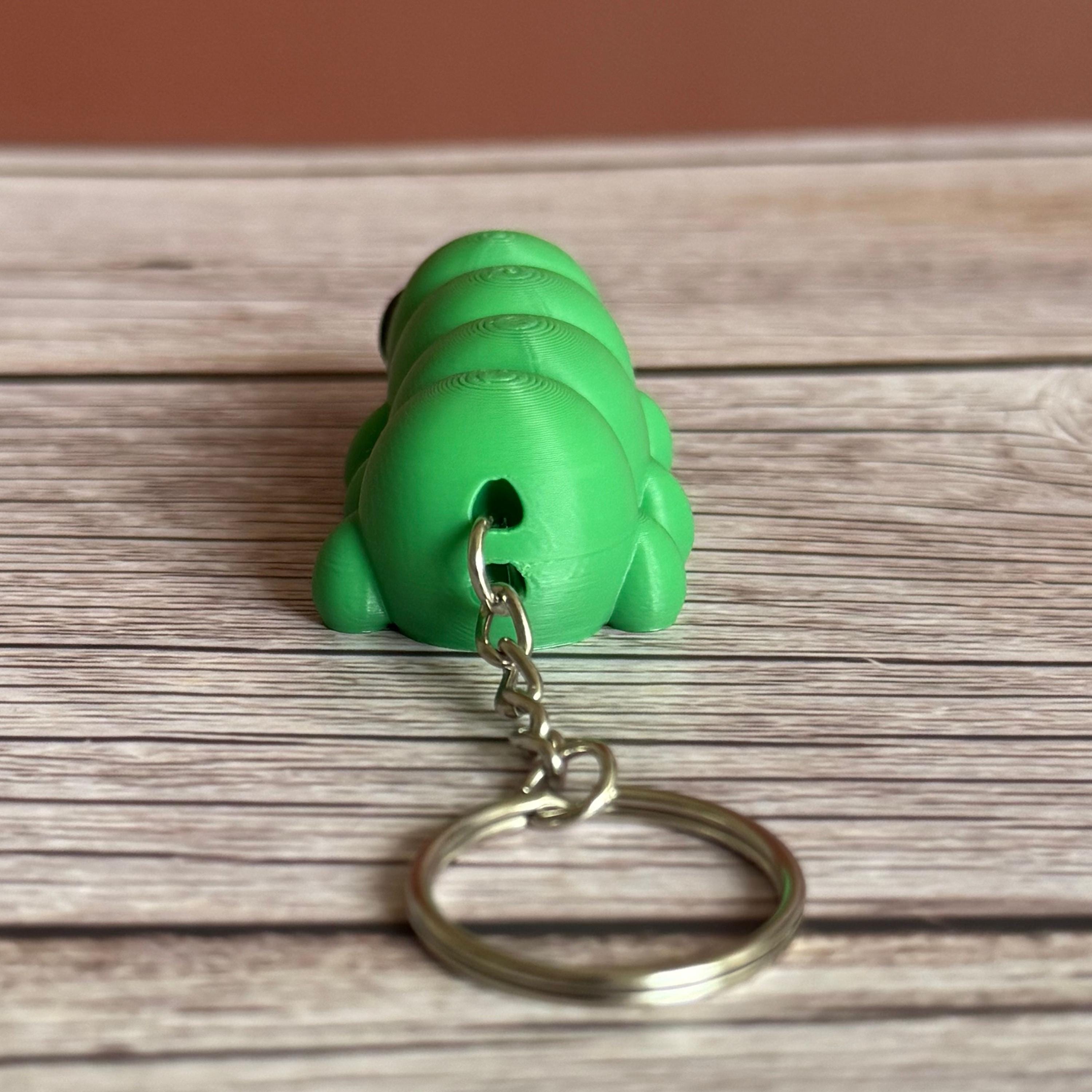 Back of a 3D printed green caterpillar-shaped keychain on a wooden surface