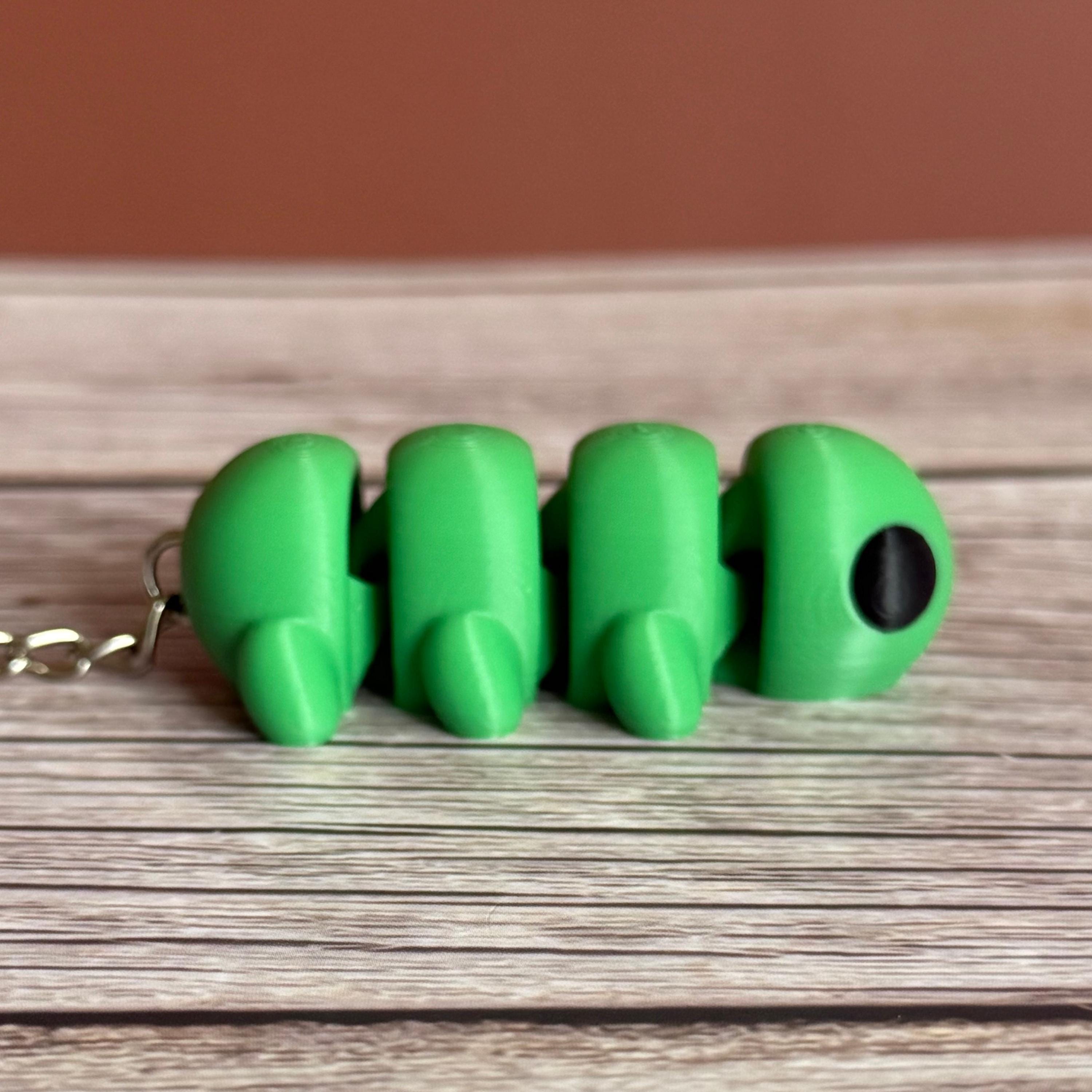 Side of a 3D printed green caterpillar-shaped keychain on a wooden surface