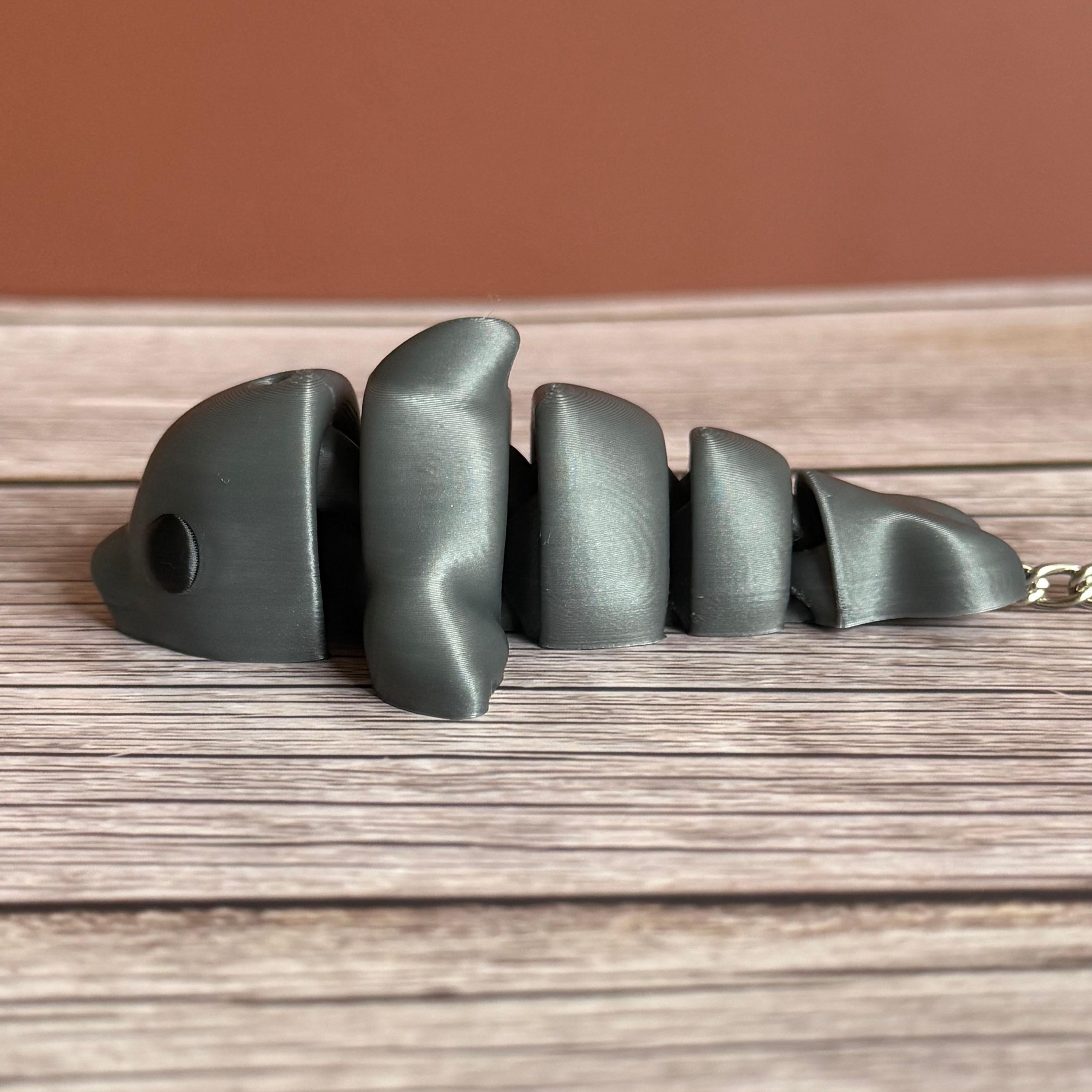 Side of a 3D printed gray dolphin-shaped keychain on a wooden surface