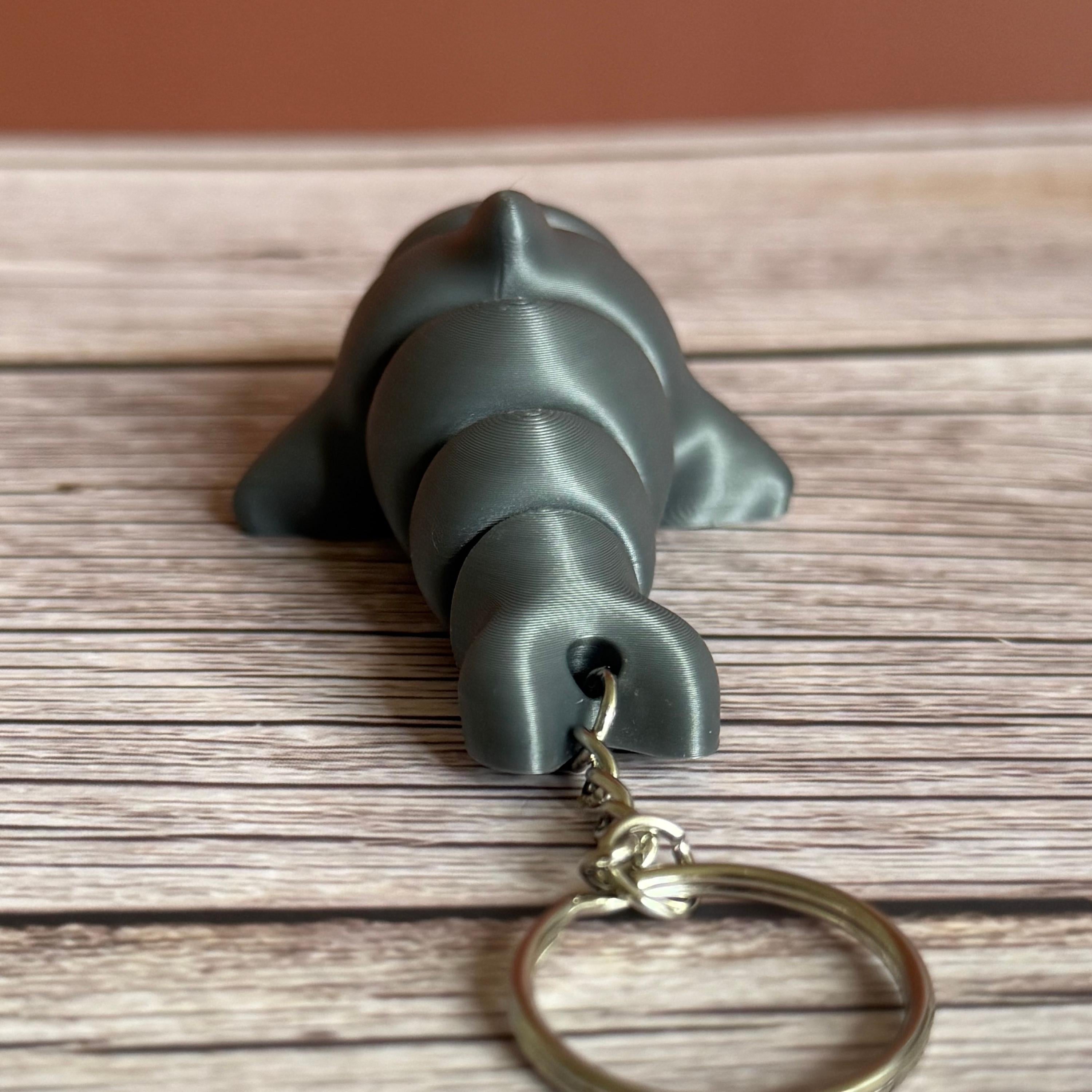 Back of a 3D printed gray dolphin-shaped keychain on a wooden surface