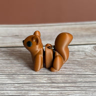 Side of a 3D printed brown squirrel-shaped keychain on a wooden surface