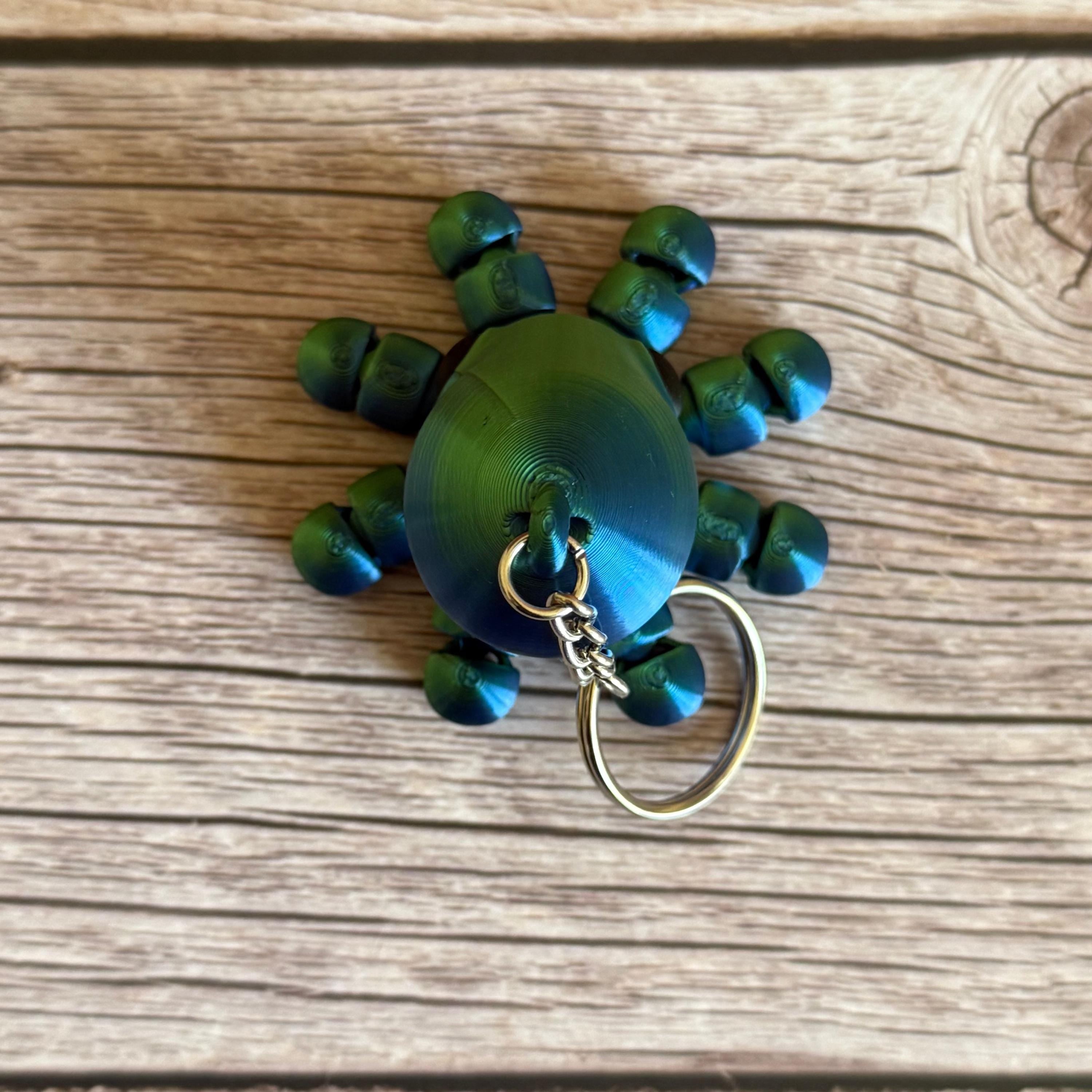 3D printed shiny green and blue octopus-shaped keychain, placed on a wooden surface