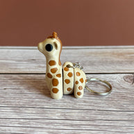 Side of 3D printed beige and brown giraffe-shaped keychain, placed on a wooden surface against a brown background