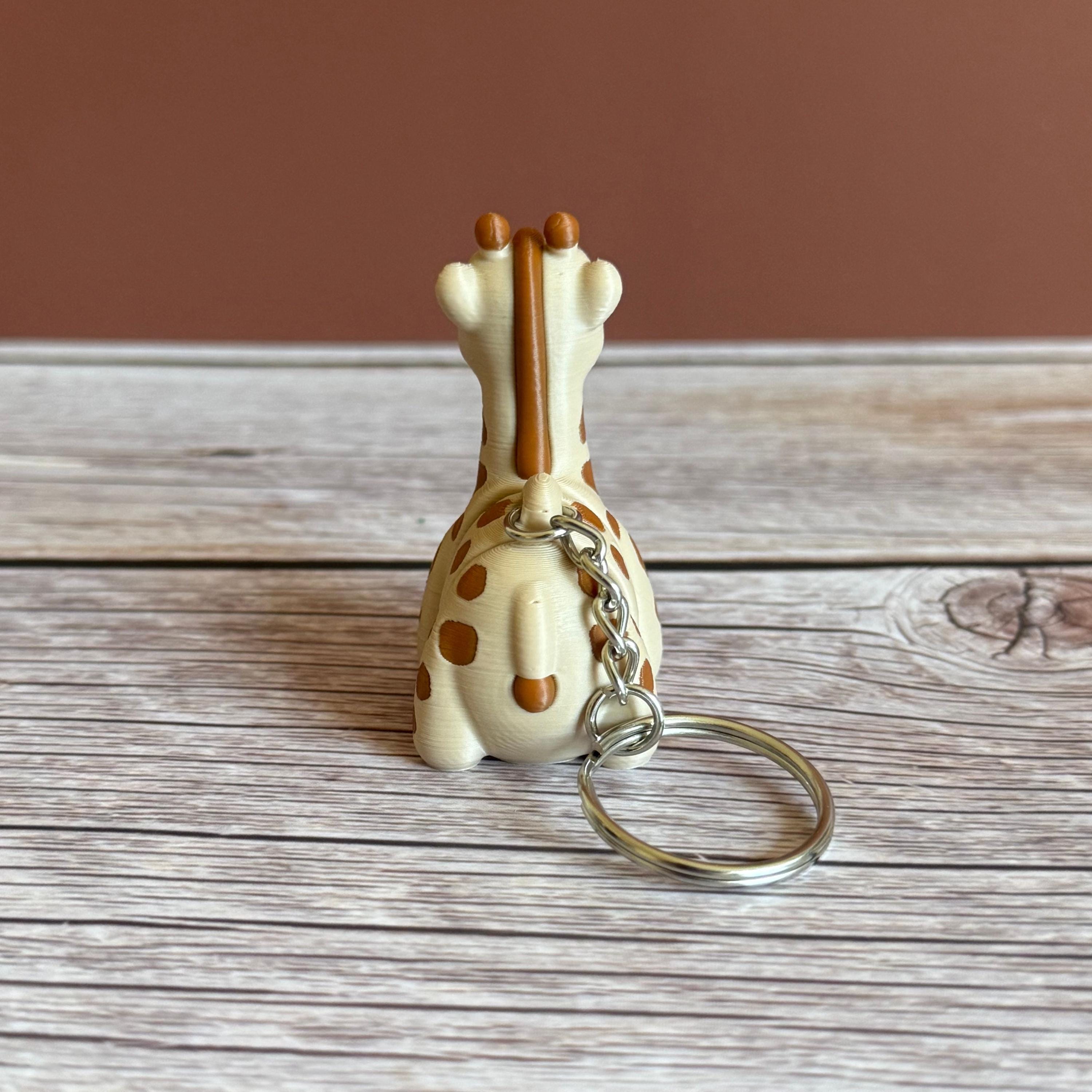 Back of 3D printed beige and brown giraffe-shaped keychain, placed on a wooden surface against a brown background