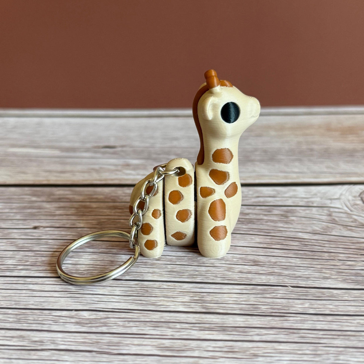 Side of 3D printed beige and brown giraffe-shaped keychain, placed on a wooden surface against a brown background