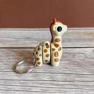 Side of 3D printed beige and brown giraffe-shaped keychain, placed on a wooden surface against a brown background