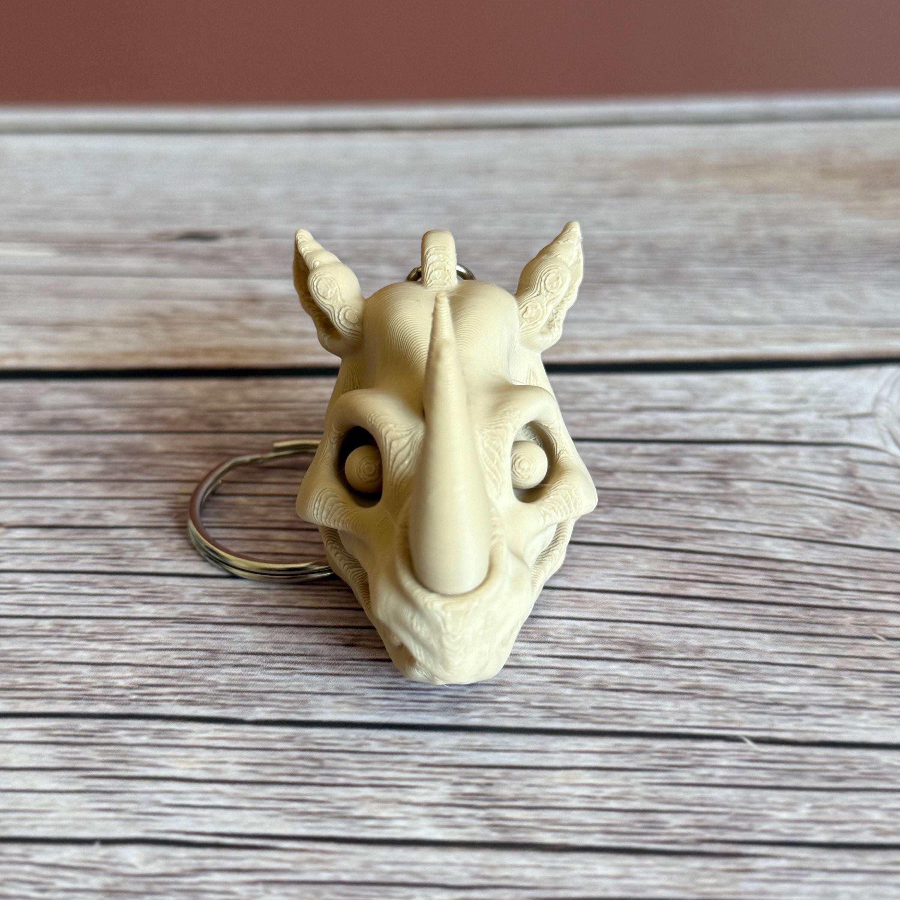 3D printed beige rhino skull keychain, placed on a wooden surface with a brown background