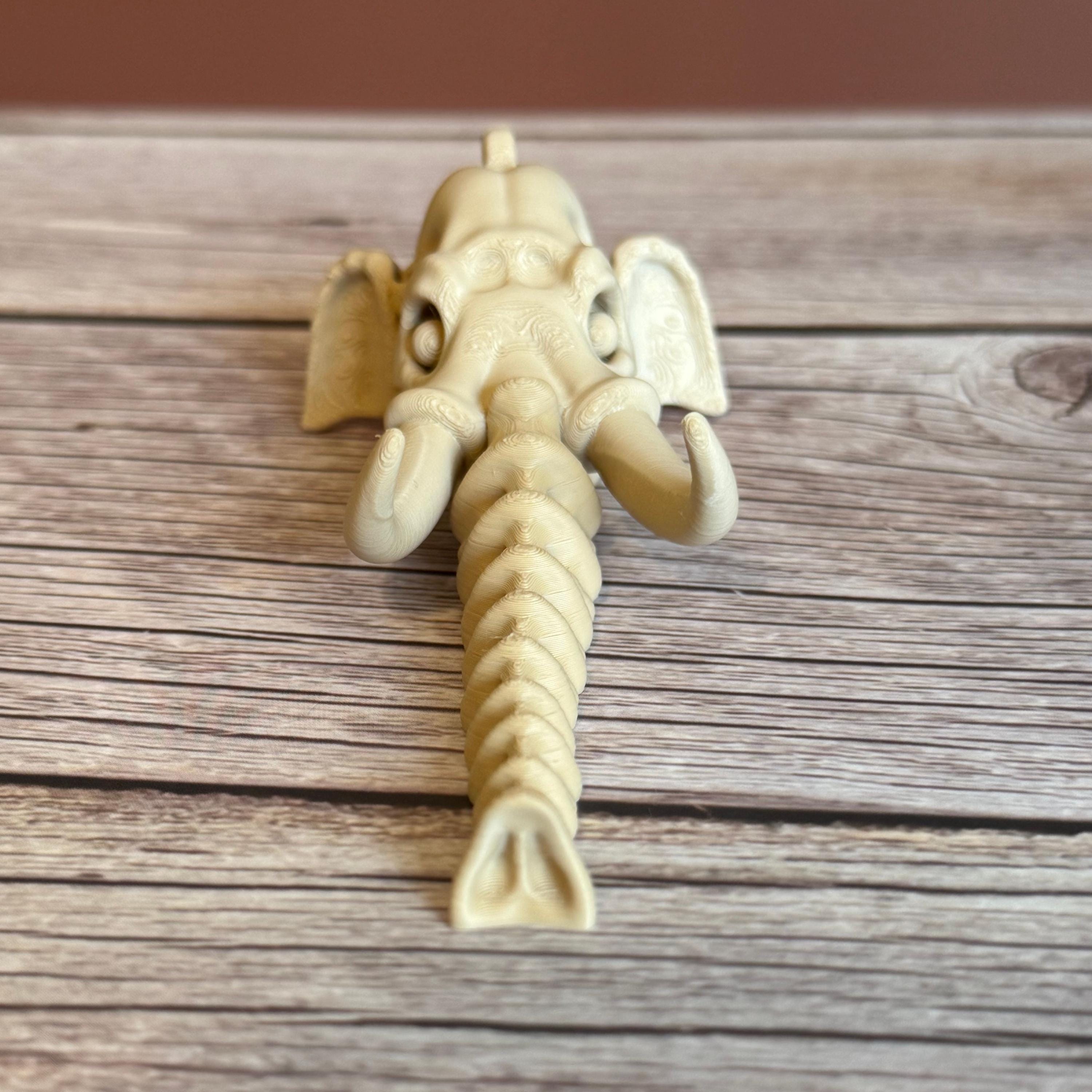 3D printed beige elephant skull with articulated skeleton-like trunk, placed on a wooden surface against a brown background